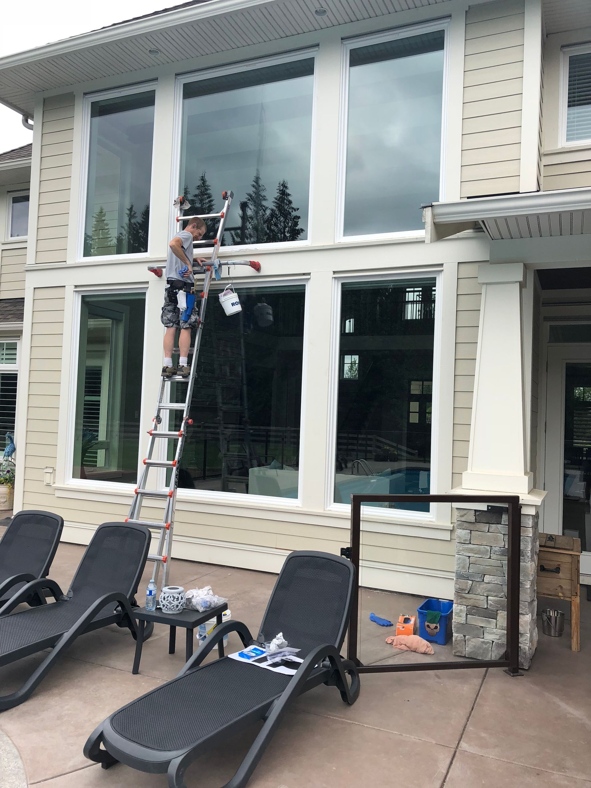 A man is standing on a ladder cleaning a window of a house.