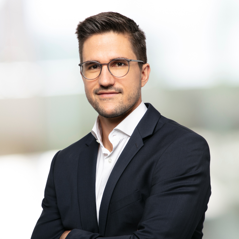 Ein Mann im Anzug und mit Brille steht mit verschränkten Armen da.