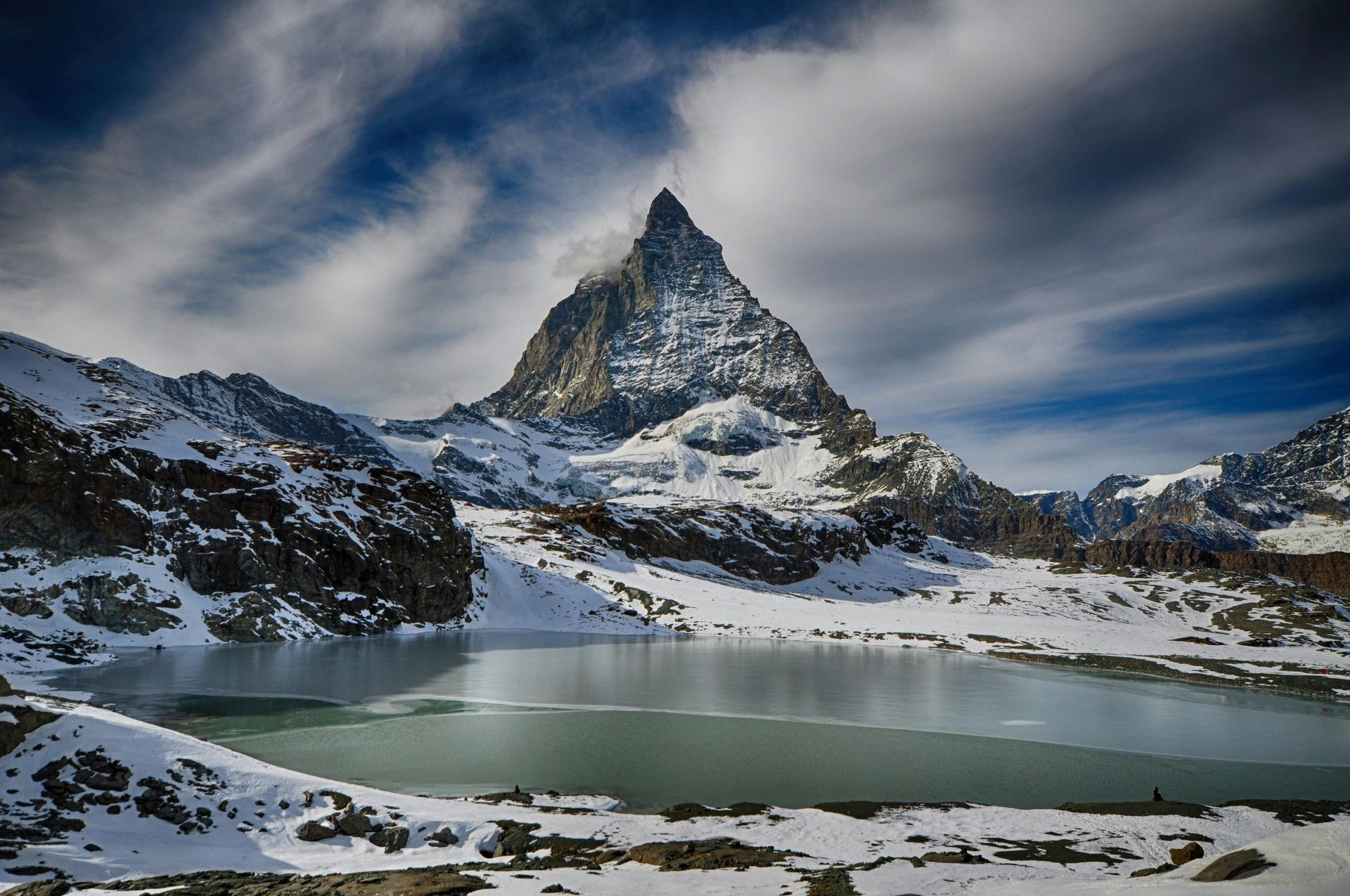 Ein schneebedeckter Berg mit einem See davor.