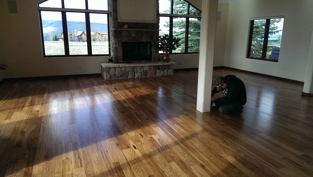 A man is kneeling in a living room with hardwood floors and a fireplace.