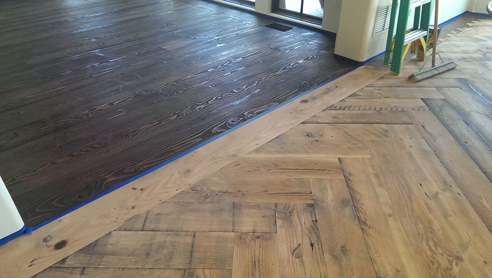 A wooden floor with a herringbone pattern is being painted in a room.