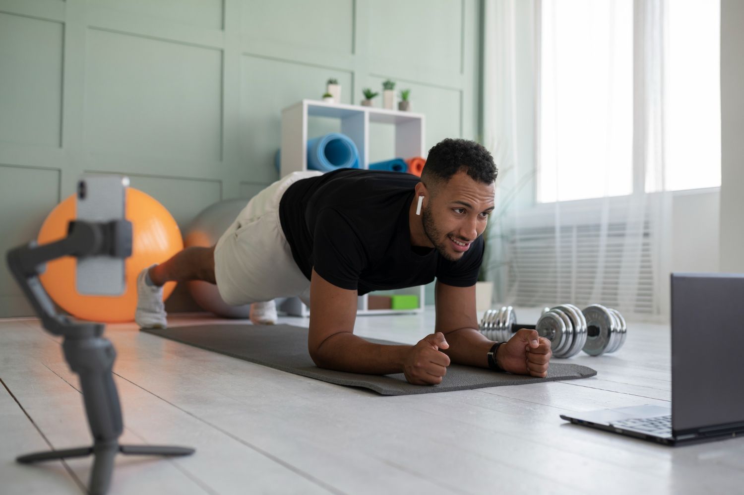 A man is doing plank exercises on a yoga mat in front of a laptop.