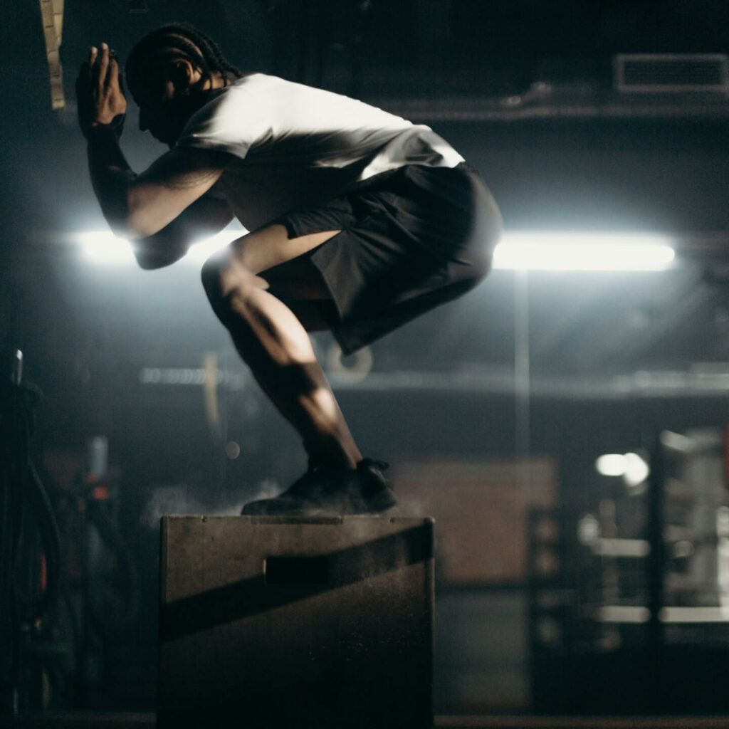 A man is squatting on a box in a dark room.