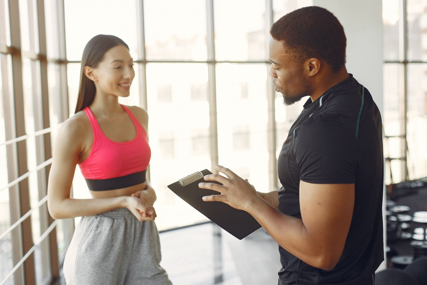 A man is talking to a woman in a gym while holding a clipboard.