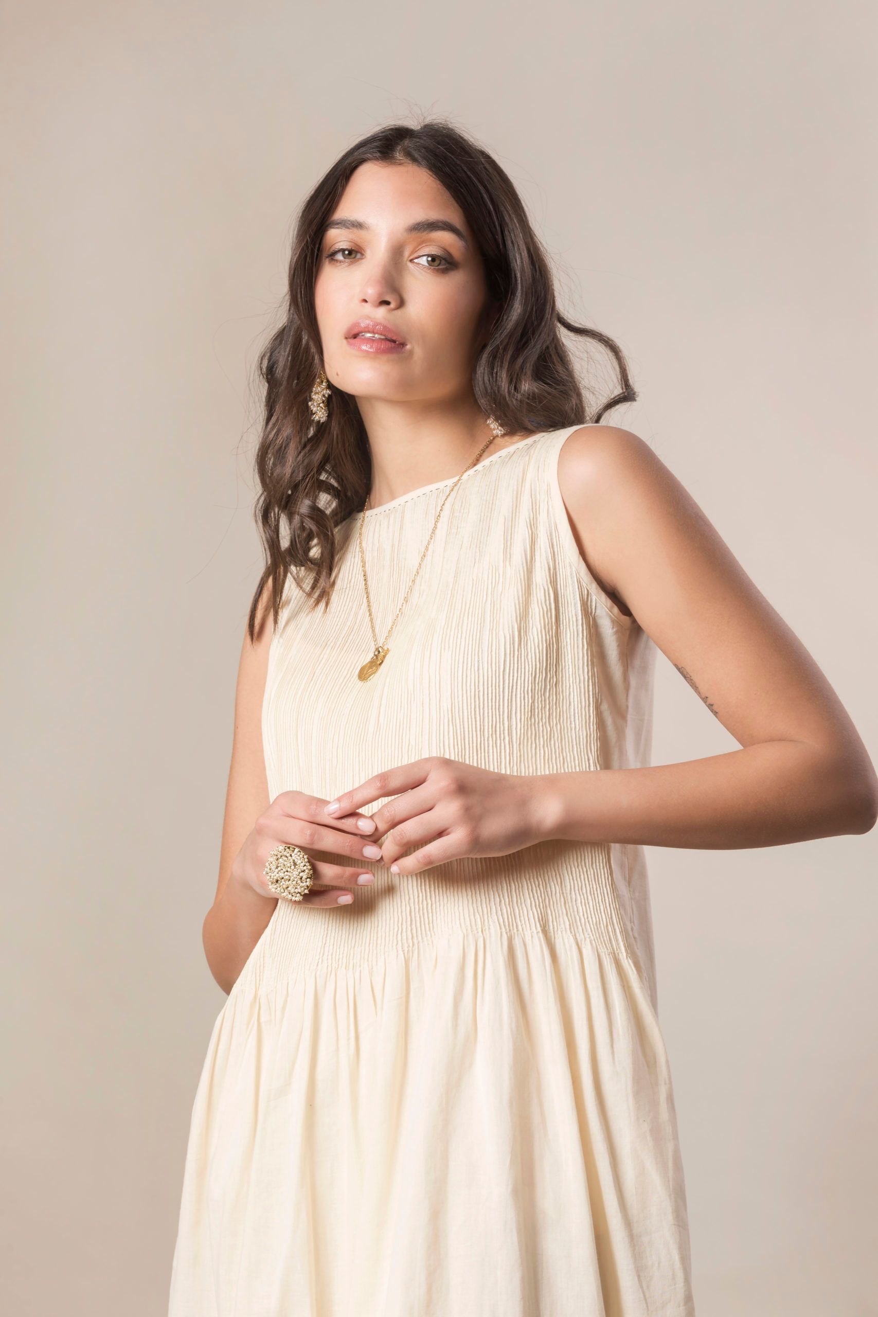 Donna con abito color crema e gioielli, che guarda verso la telecamera.