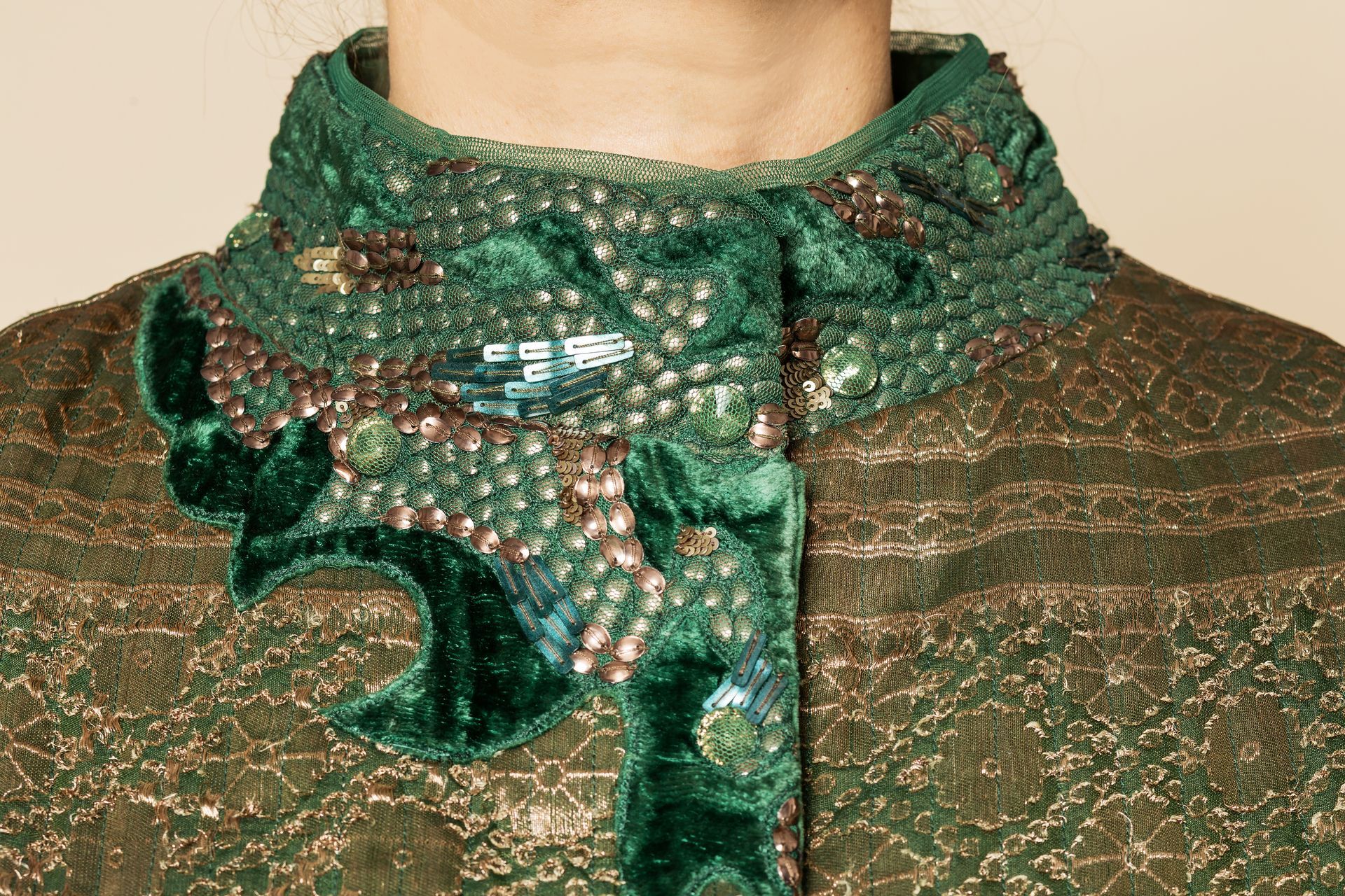 Primo piano di un colletto in velluto verde con perline e decorazioni elaborate su una giacca verde con fantasia.