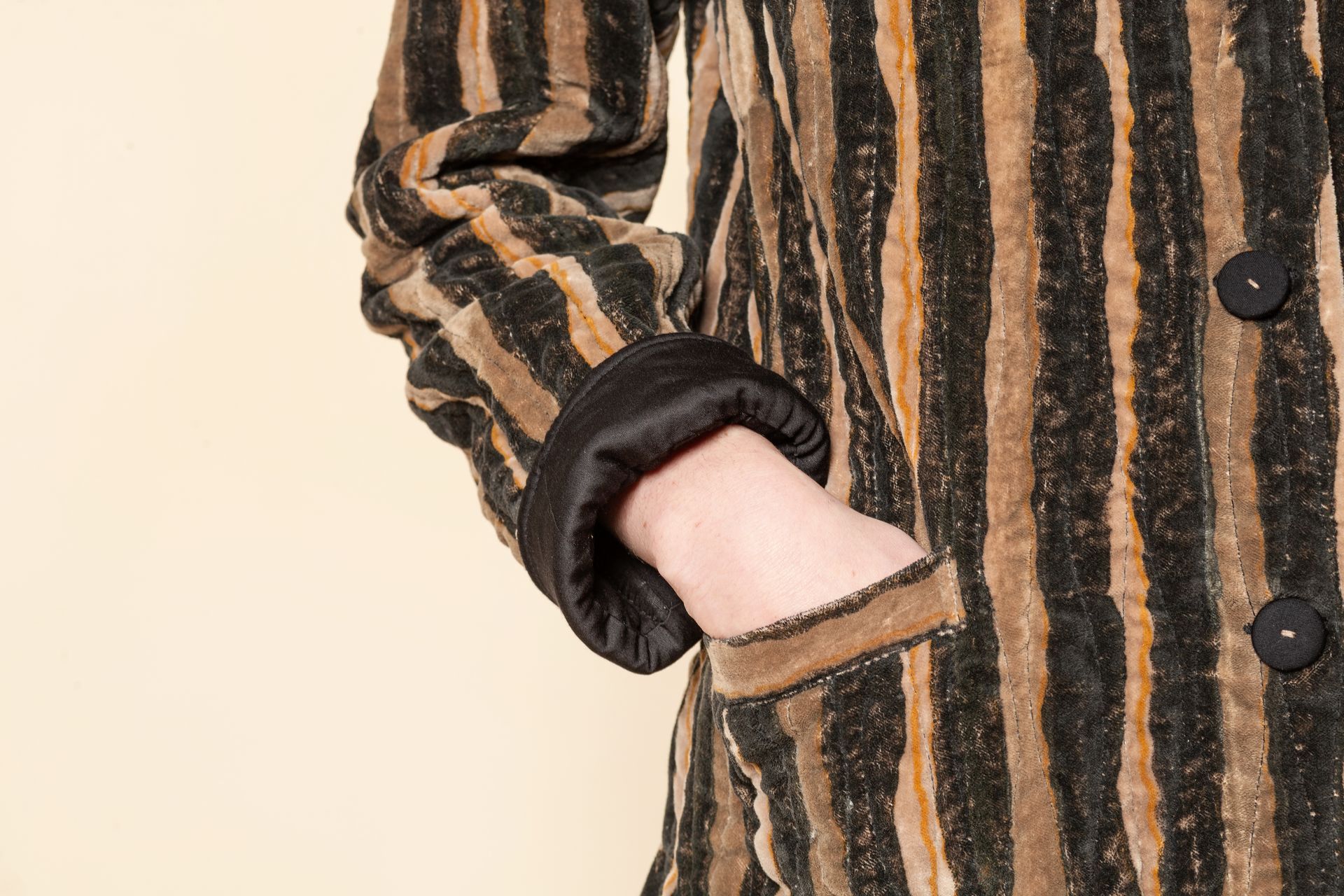 Braccio in cappotto a righe marrone e nero con polsino scuro.