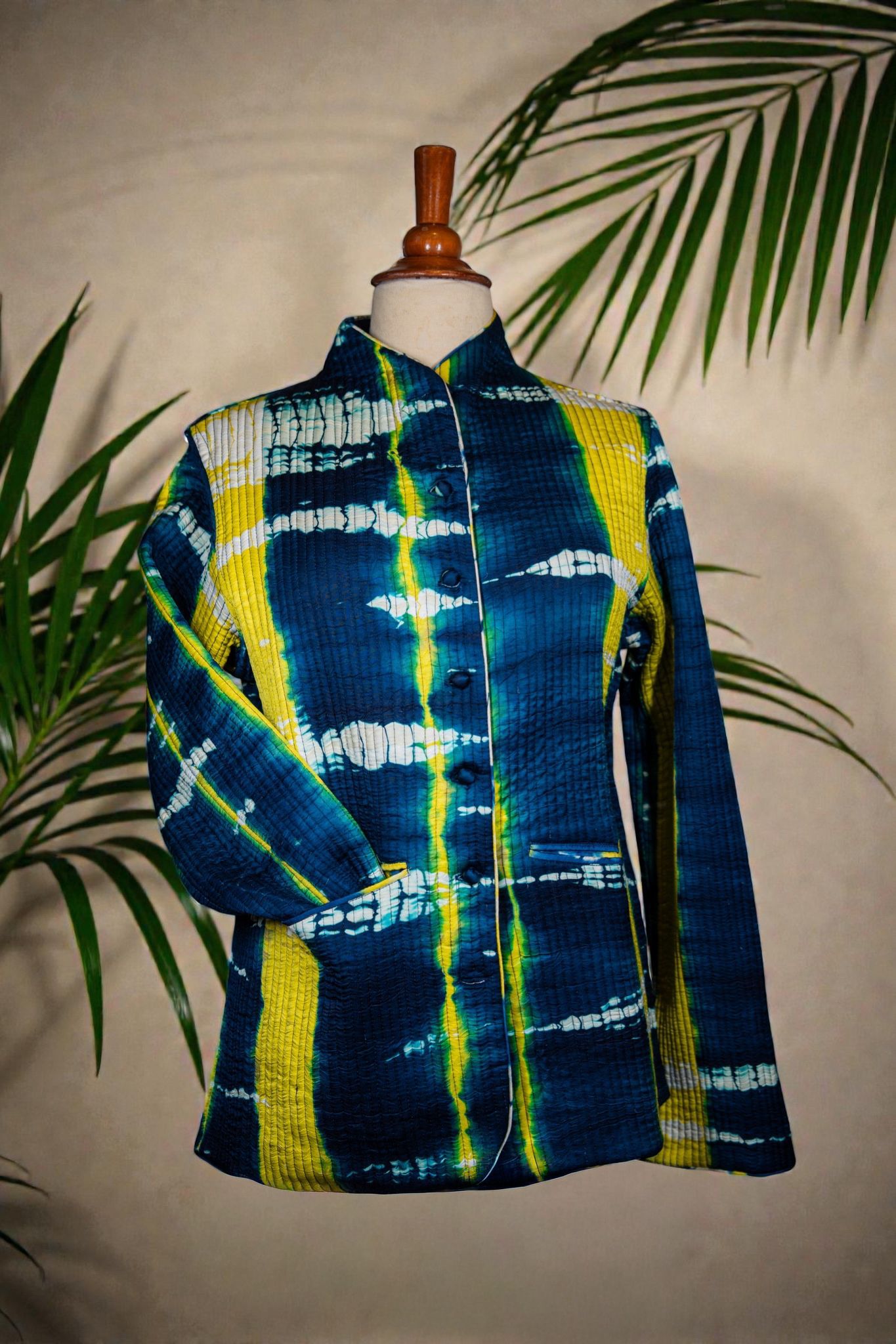 Giacca trapuntata a maniche lunghe con bottoni, caratterizzata da una fantasia tie-dye blu e gialla su un manichino.