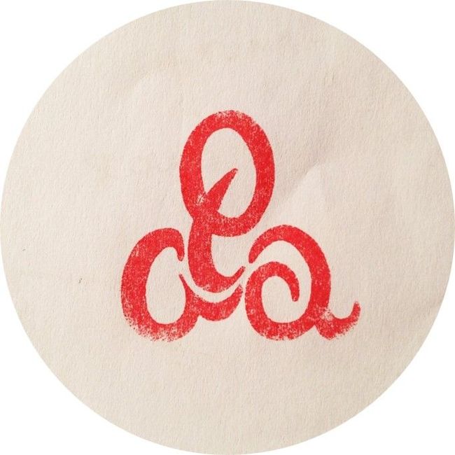 Donna in un magazzino di tappeti con in mano un articolo decorato, circondata da pile di tappeti e tessuti.