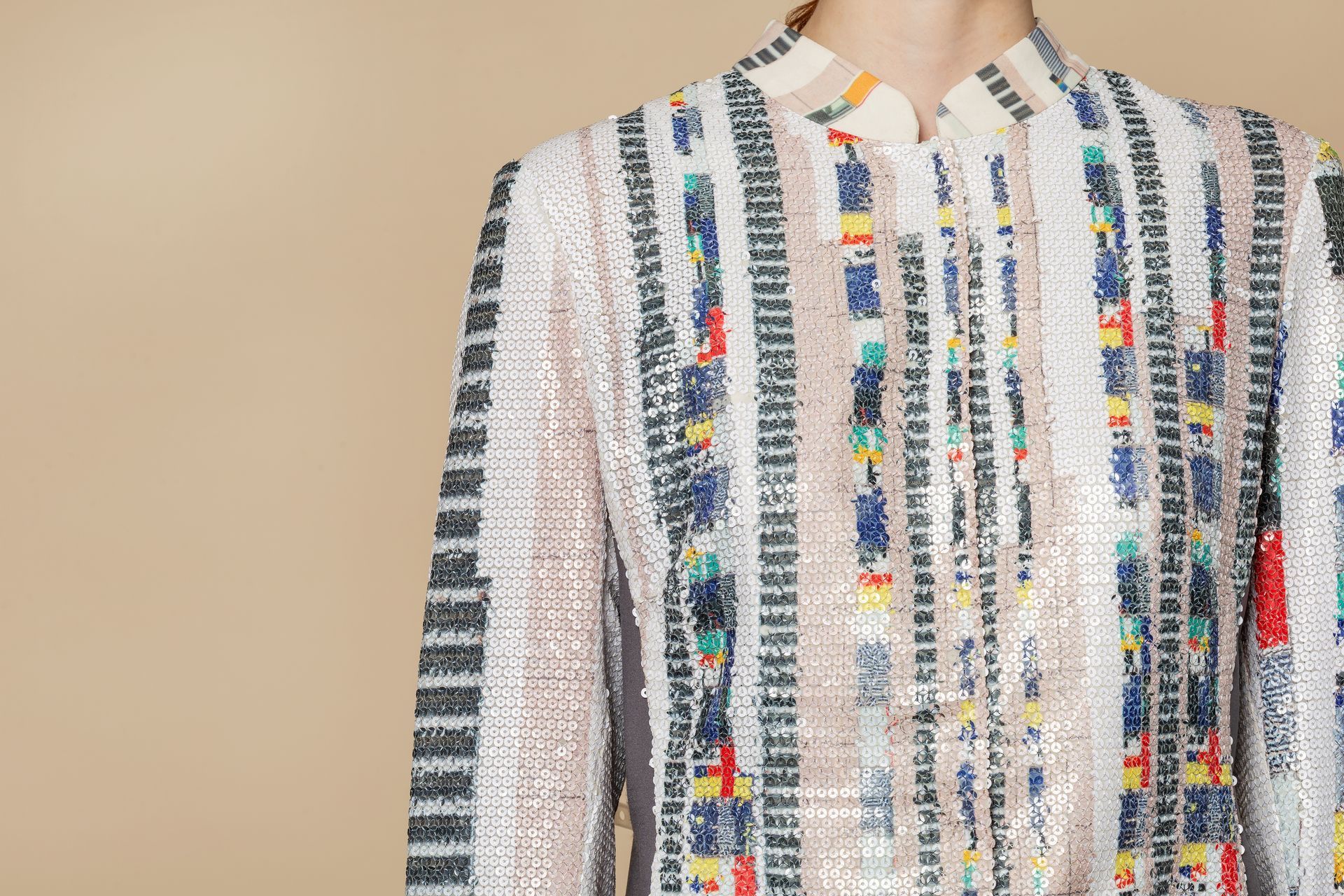 Giacca di paillettes con righe verticali e blocchi colorati; sfondo neutro.