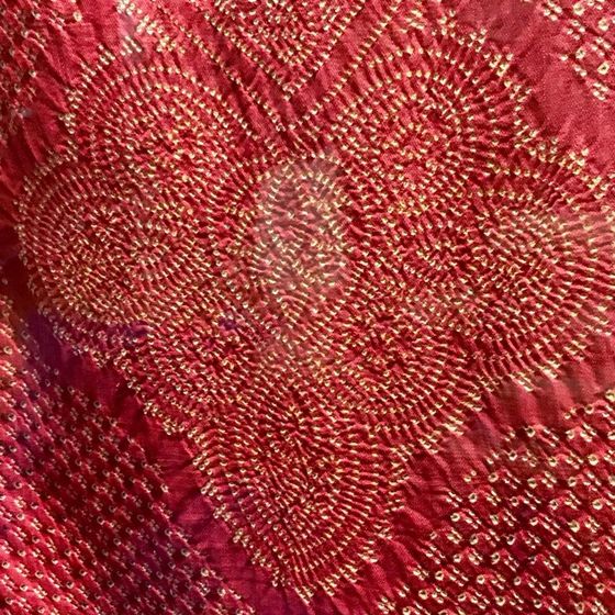 Primo piano di tessuto rosso con ricami circolari dorati che formano un disegno a cuore.