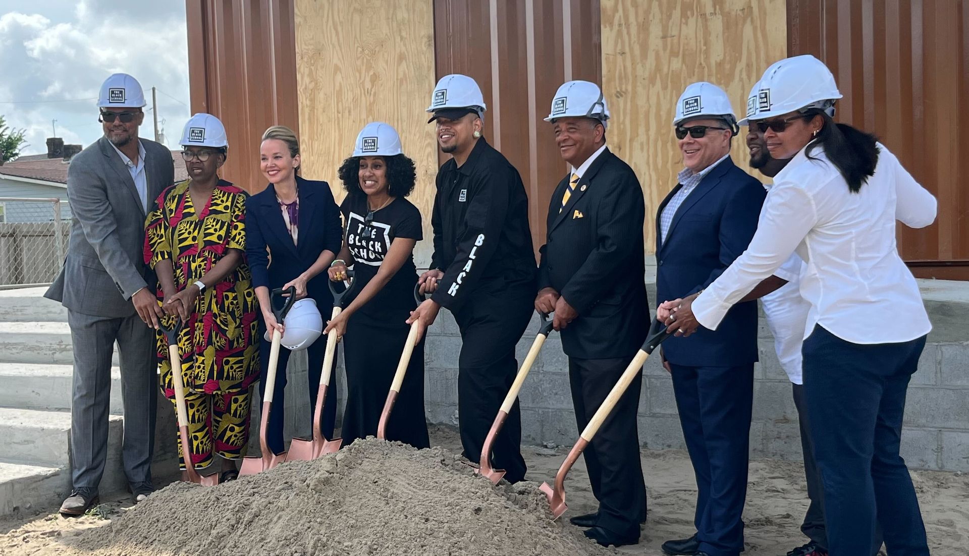 People in hard hats use shovels for groundbreaking ceremony.