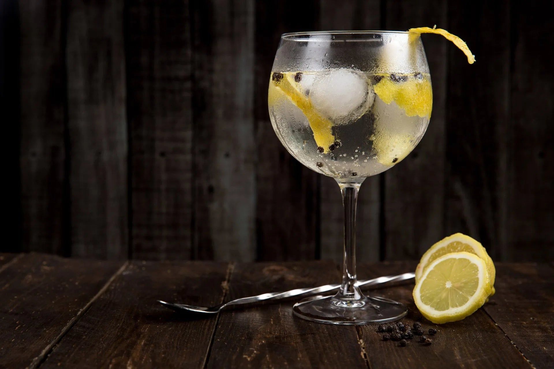 A glass of gin and tonic with ice and lemon slices on a wooden table.