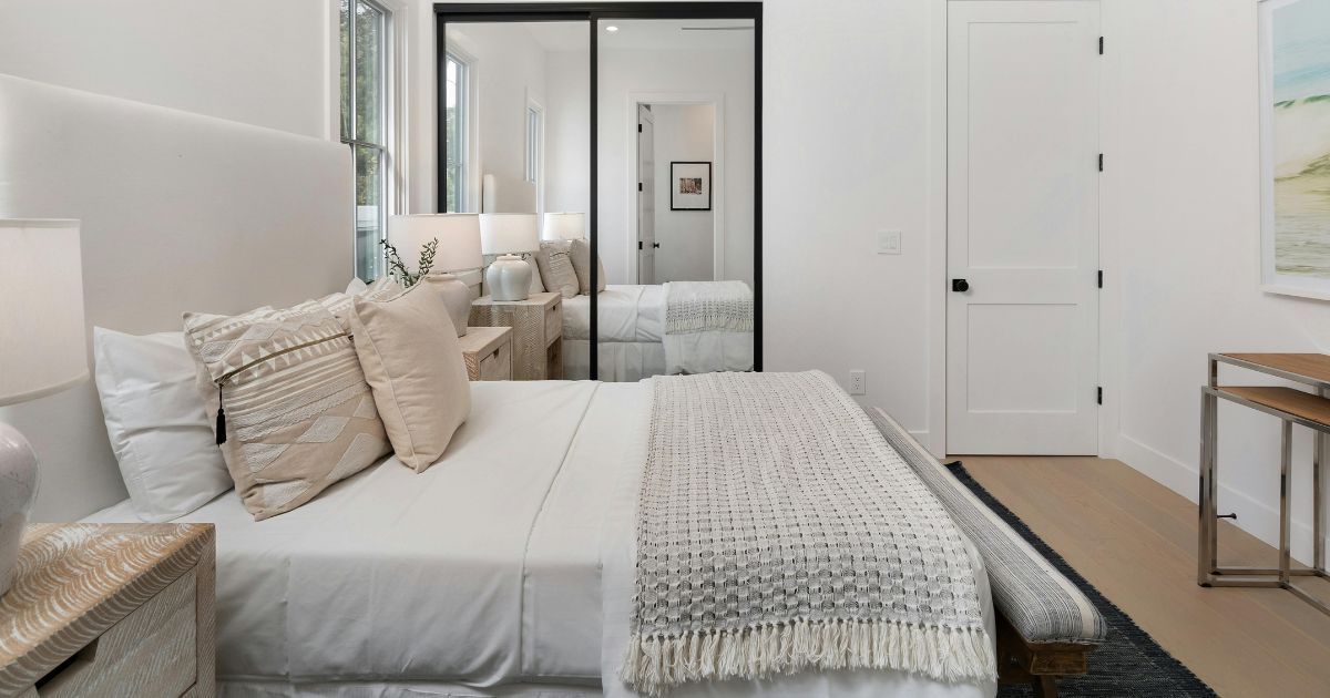 Bedroom with a large white bed, decorative pillows, and a mirrored closet door.