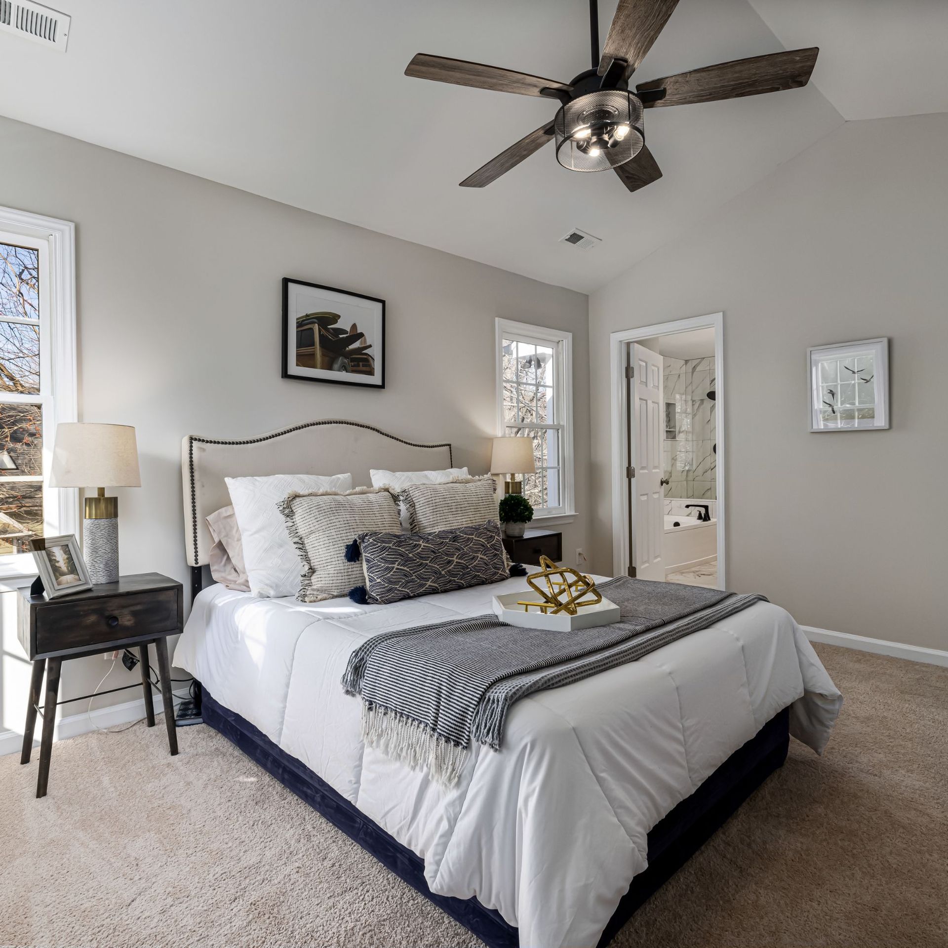 Bedroom with bed, nightstands, and a ceiling fan. Neutral color palette with small framed art.