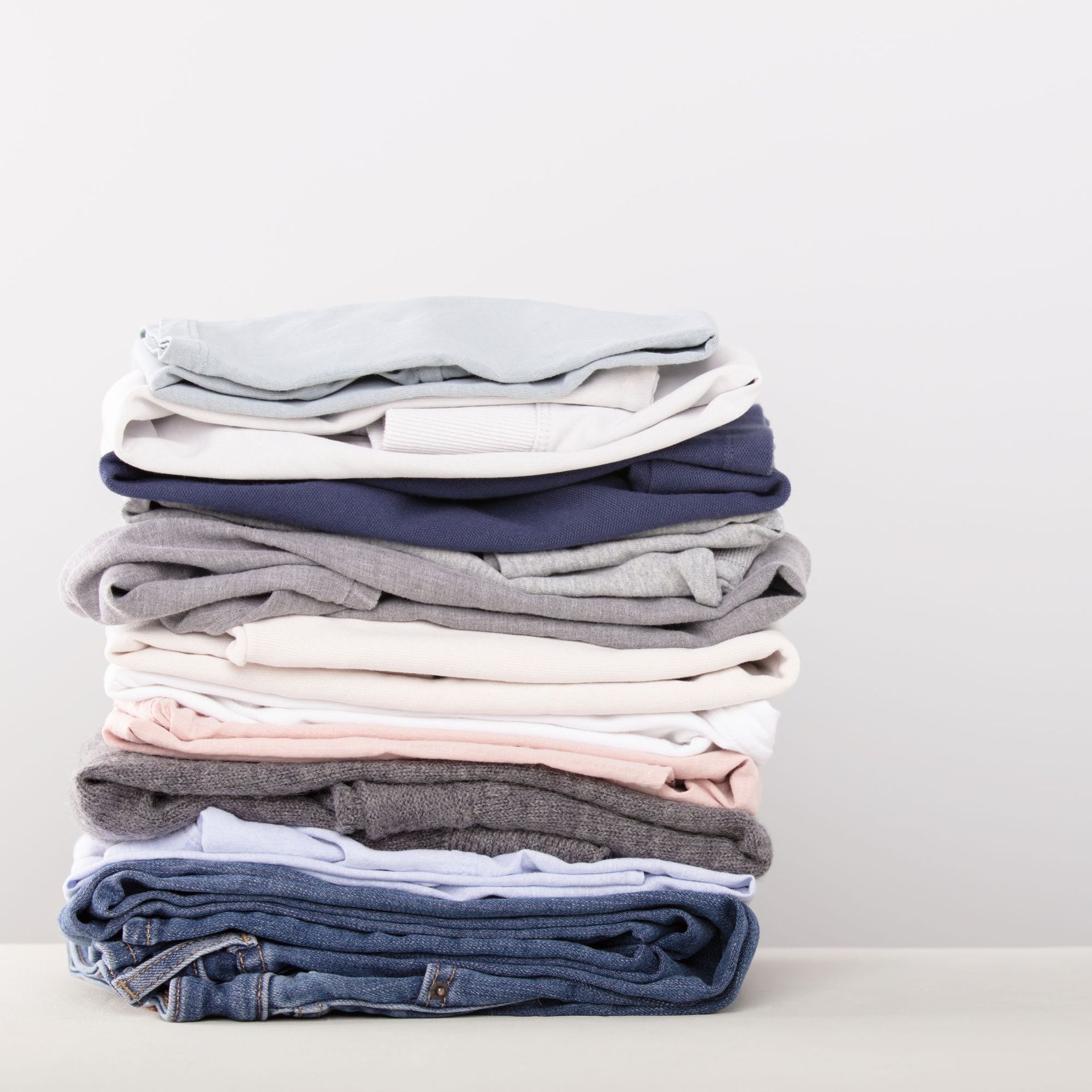 Stack of folded clothing in various colors on a white surface.