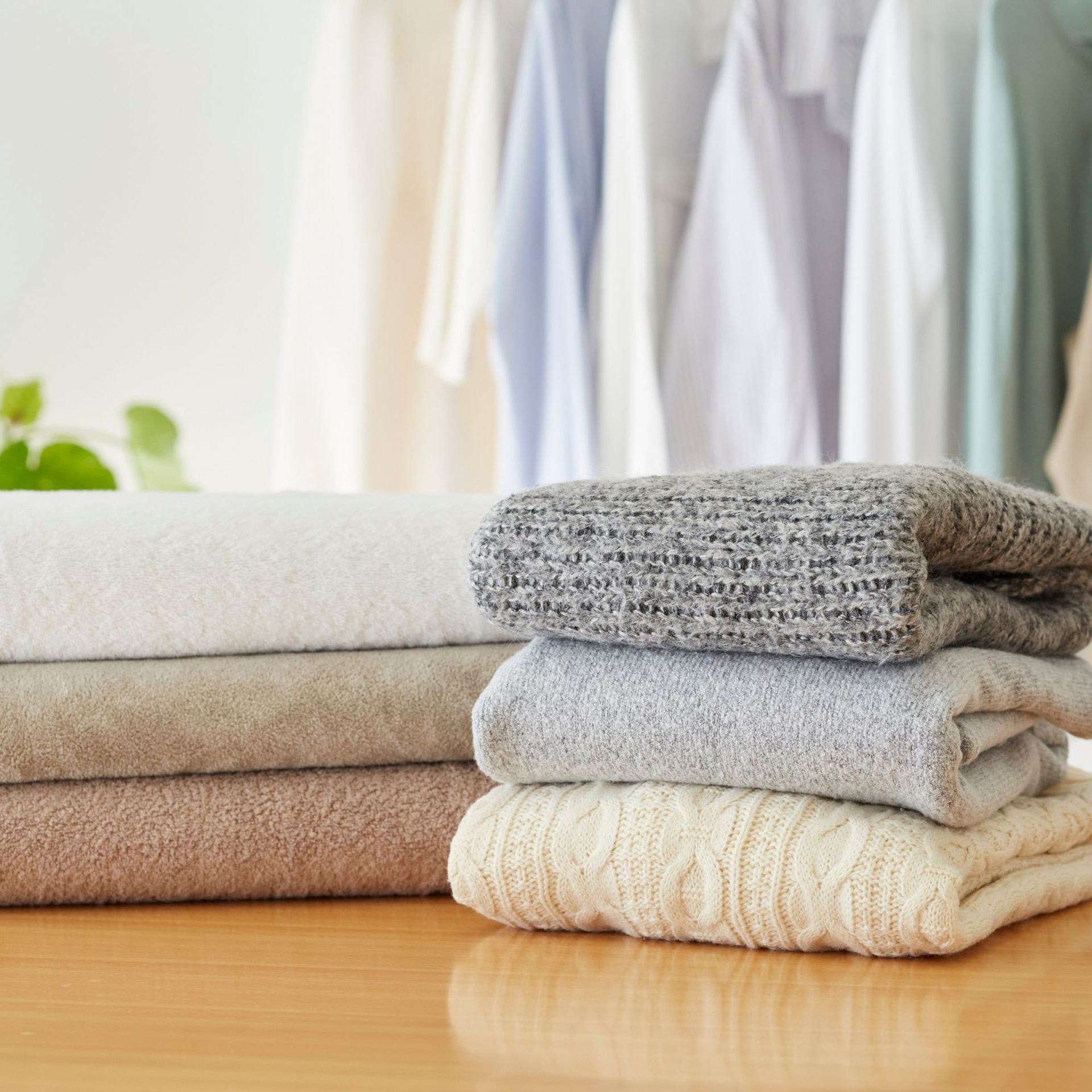 Stacks of folded blankets in various neutral colors, clothes hanging in background.