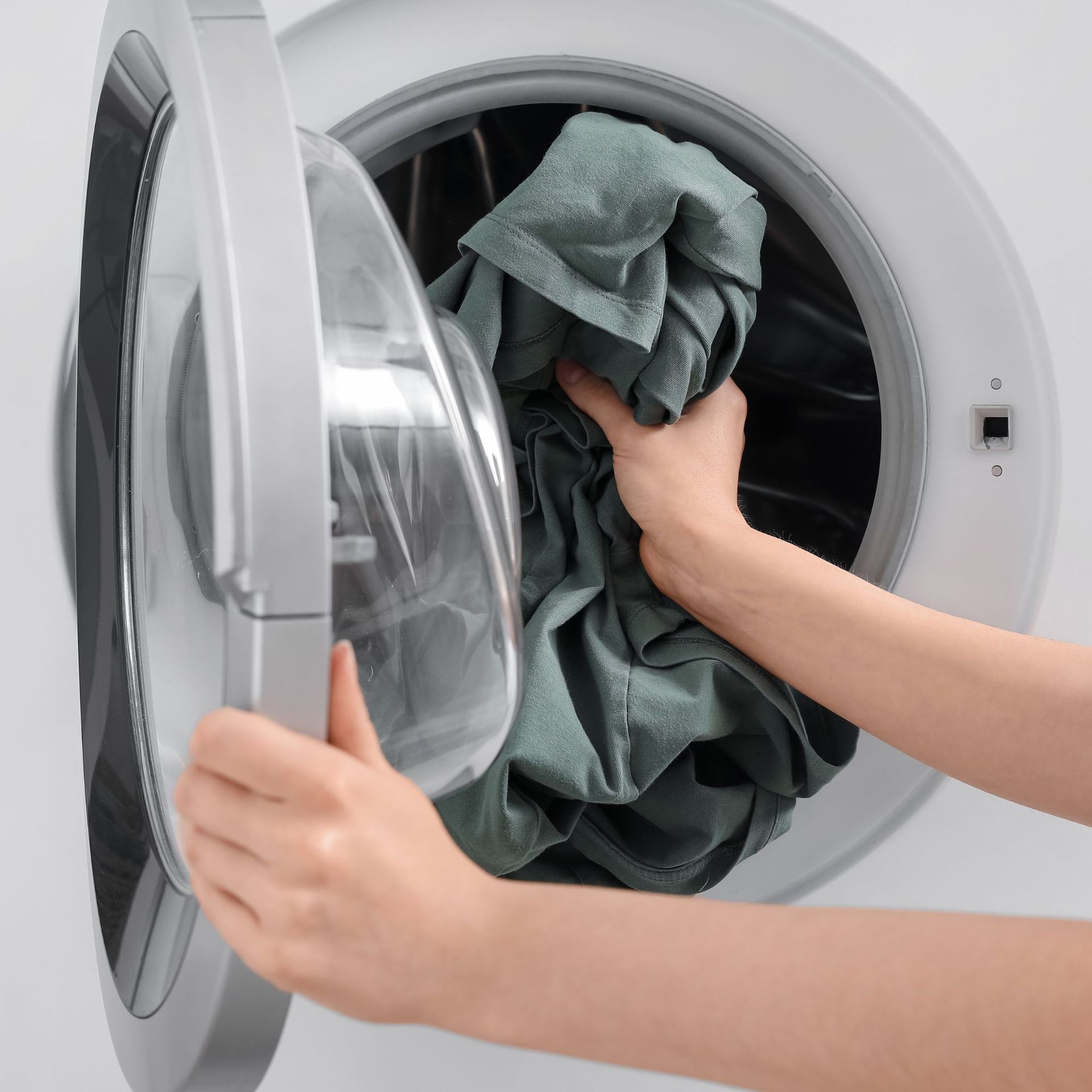 Person loading green clothes into a white washing machine.