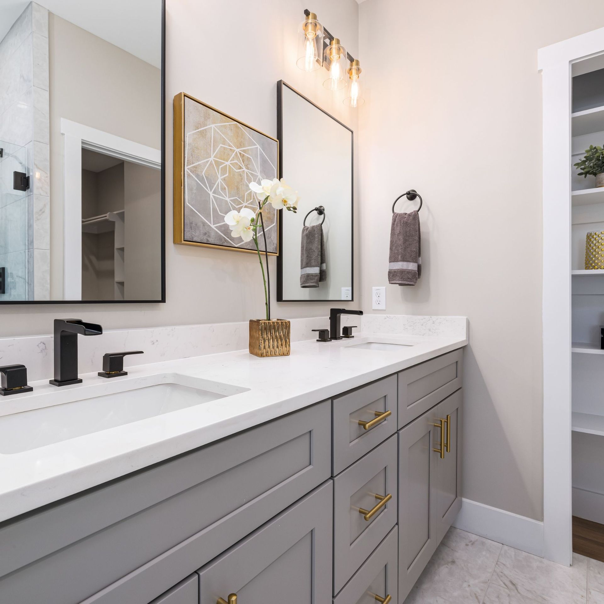 Gray and white bathroom with double vanity, gold fixtures, and framed mirrors.