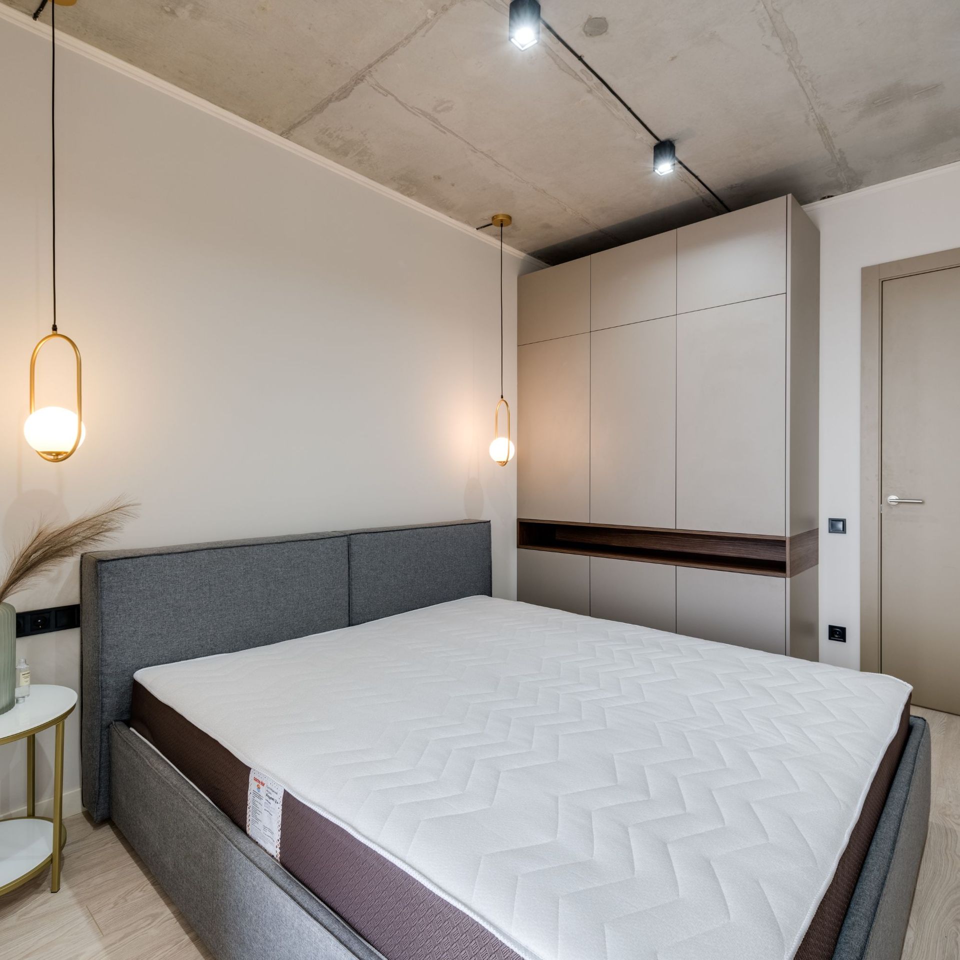 Bedroom with a grey bed, large closet, hanging lights, and concrete ceiling.
