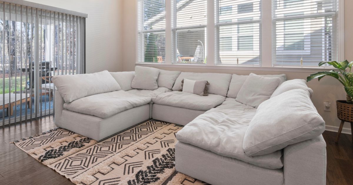 Living room with a large white sectional sofa on a patterned rug; large windows and sliding glass door.