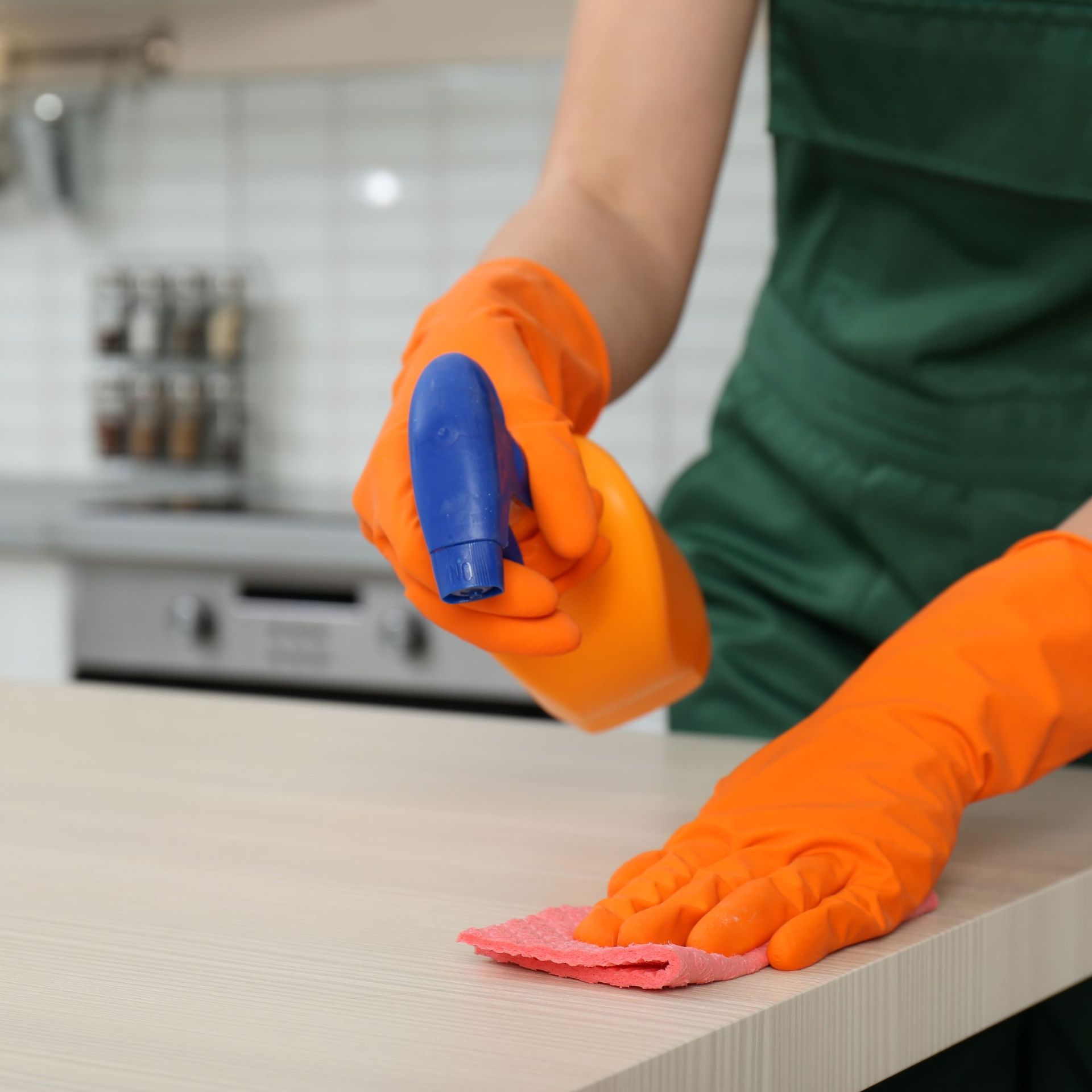 Person in orange gloves cleaning a kitchen counter with spray bottle and cloth.