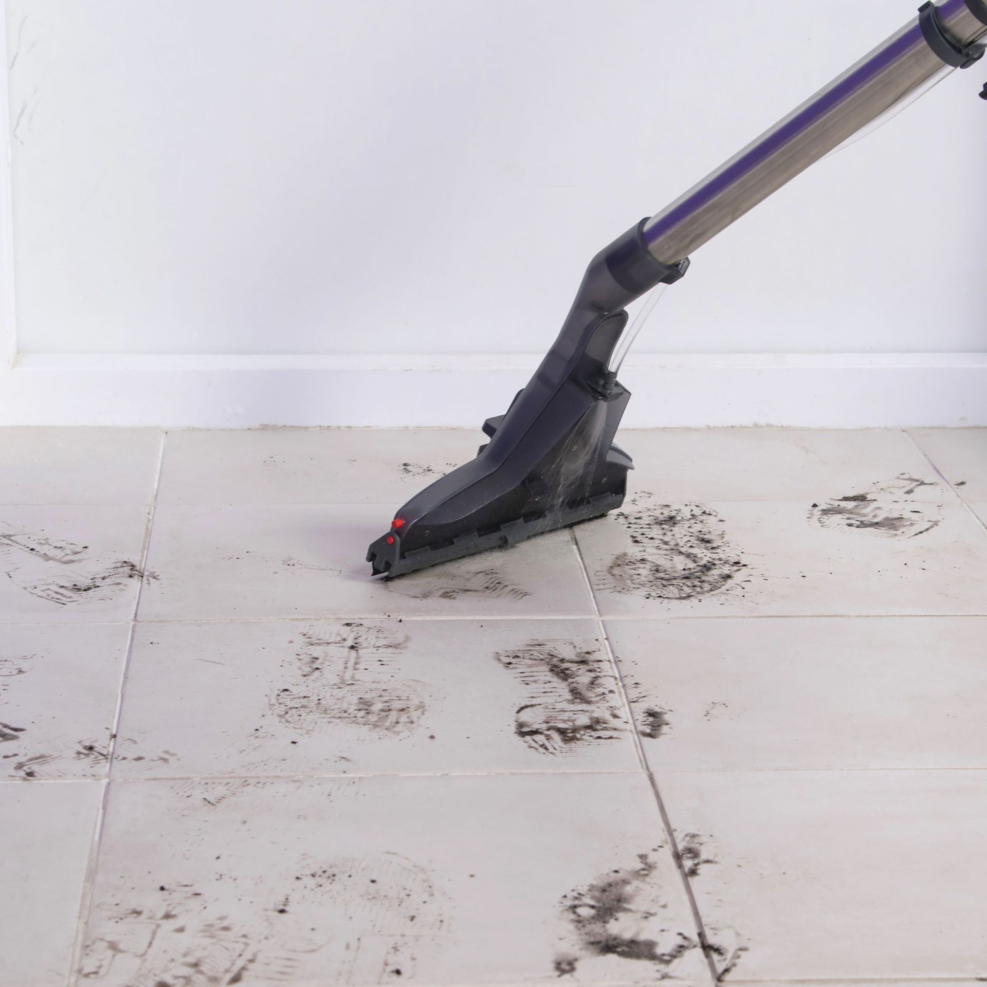Vacuum cleaner cleaning muddy footprints on tiled floor.
