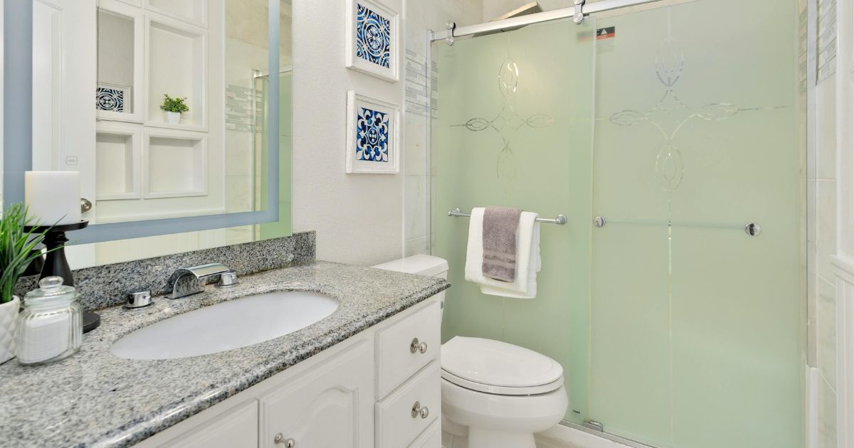 Bathroom with white vanity, granite countertop, frosted glass shower, and blue decor.