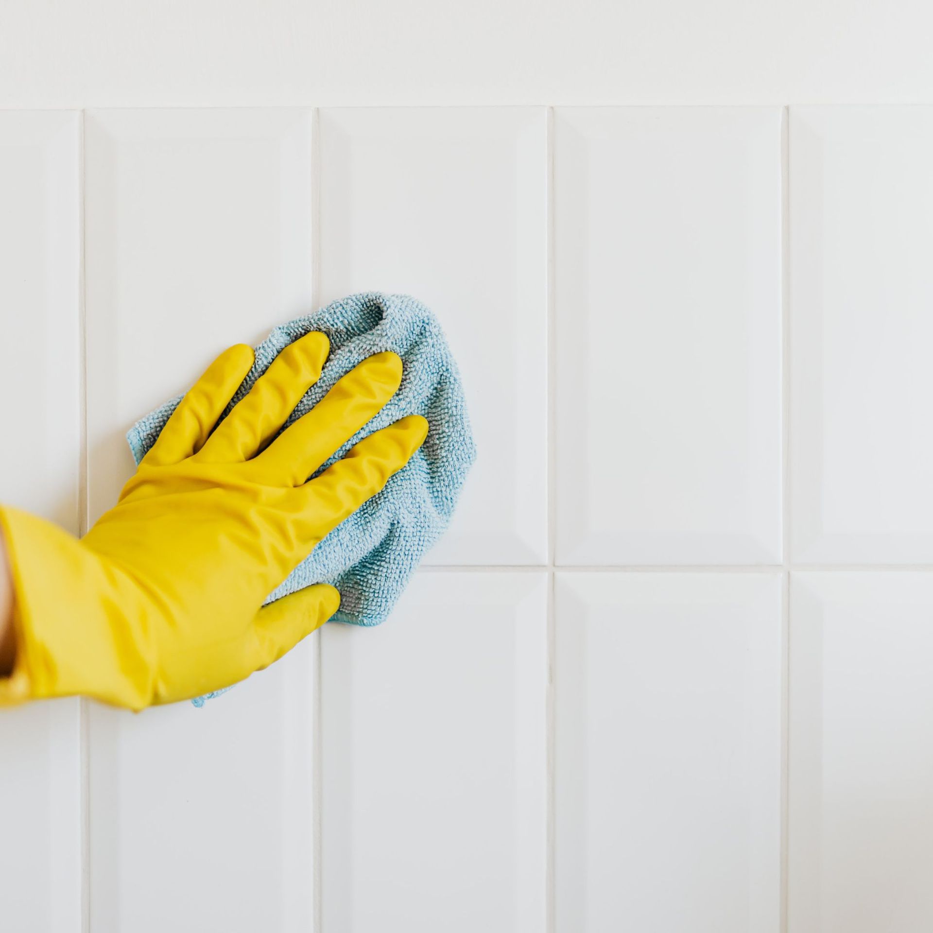 Yellow-gloved hand wiping a blue cloth on white tile wall.