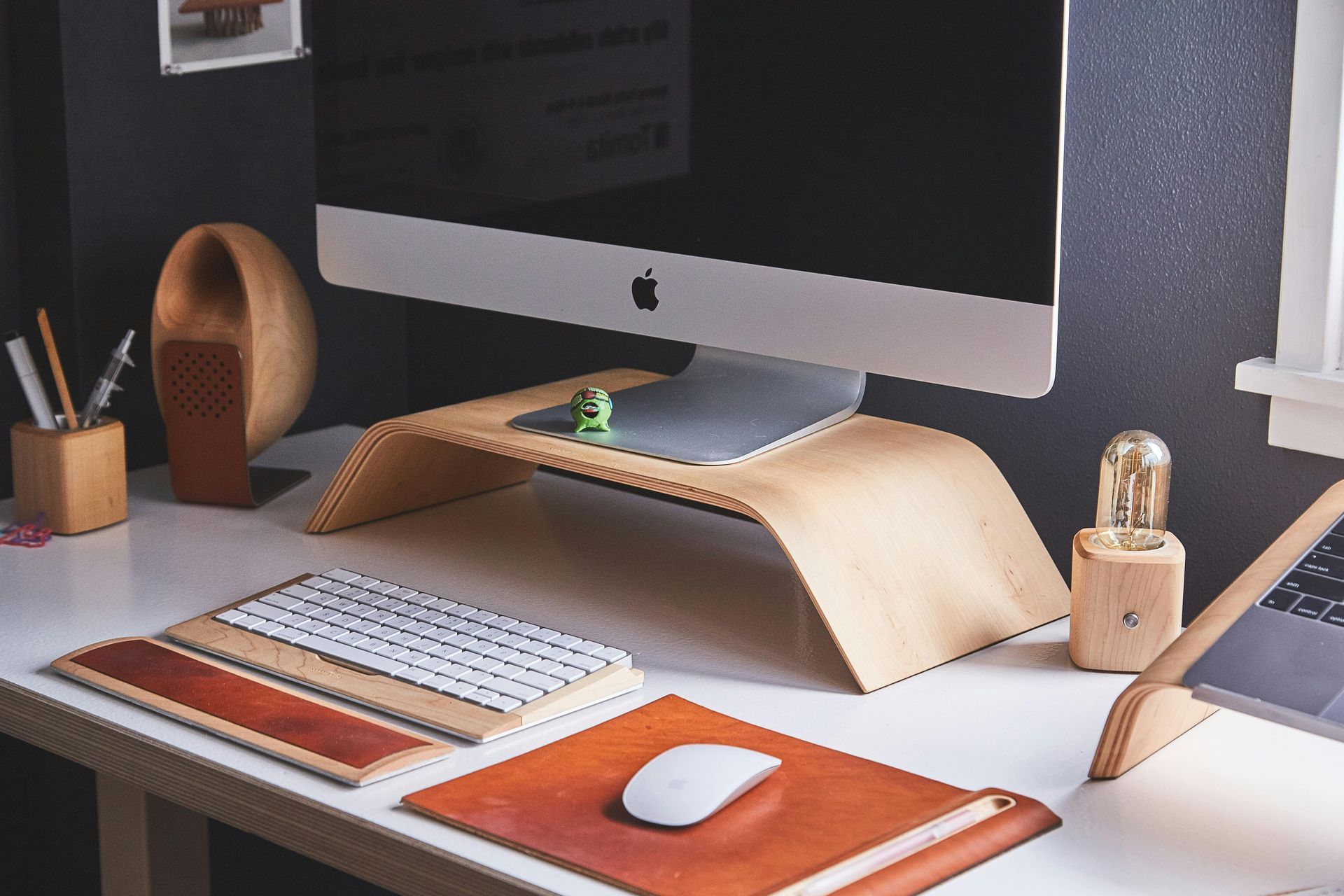 A modern desk setup with a computer, wooden accessories, and a white mouse on a leather mat.