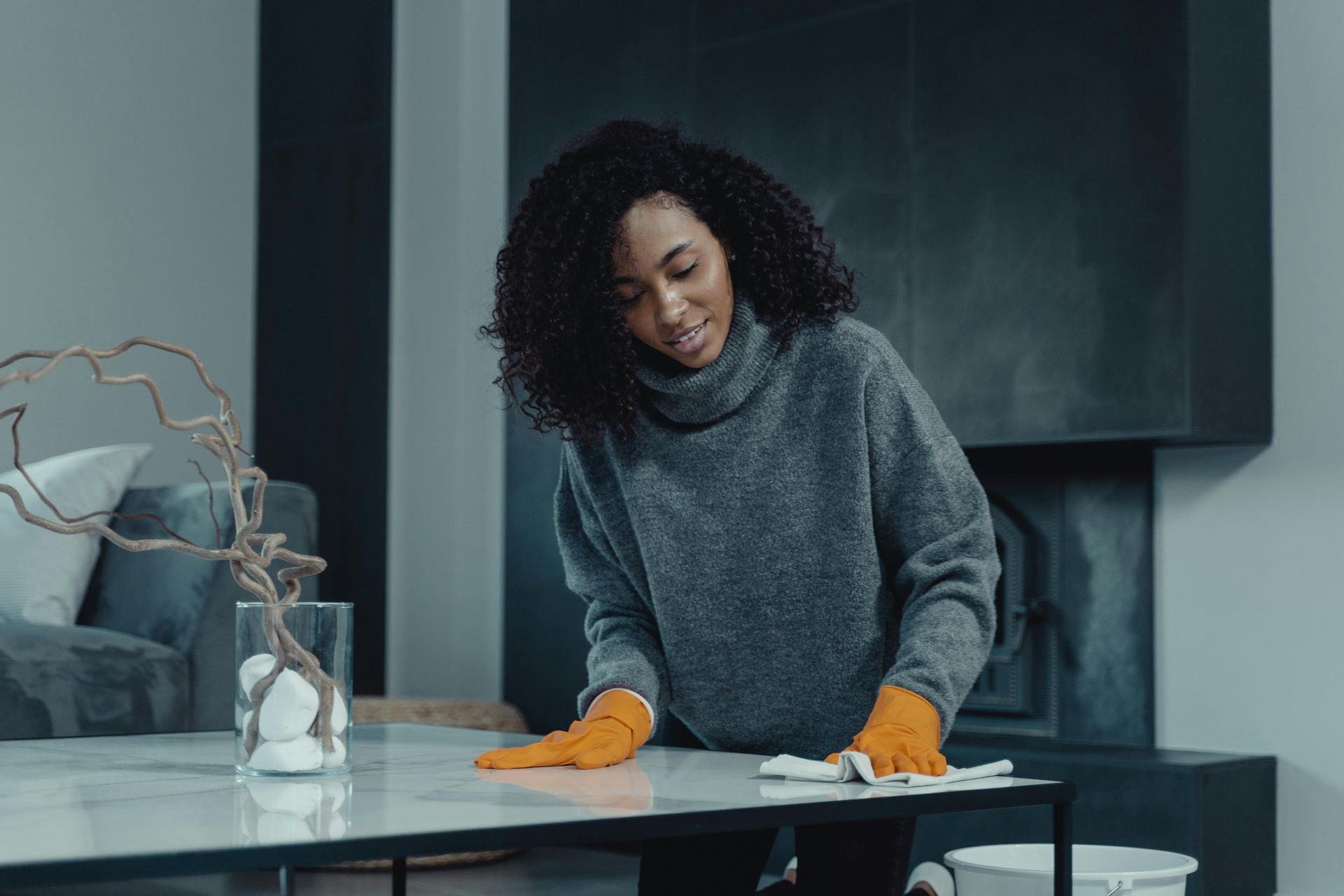 Woman wearing gloves, cleaning a marble-topped table with a cloth.