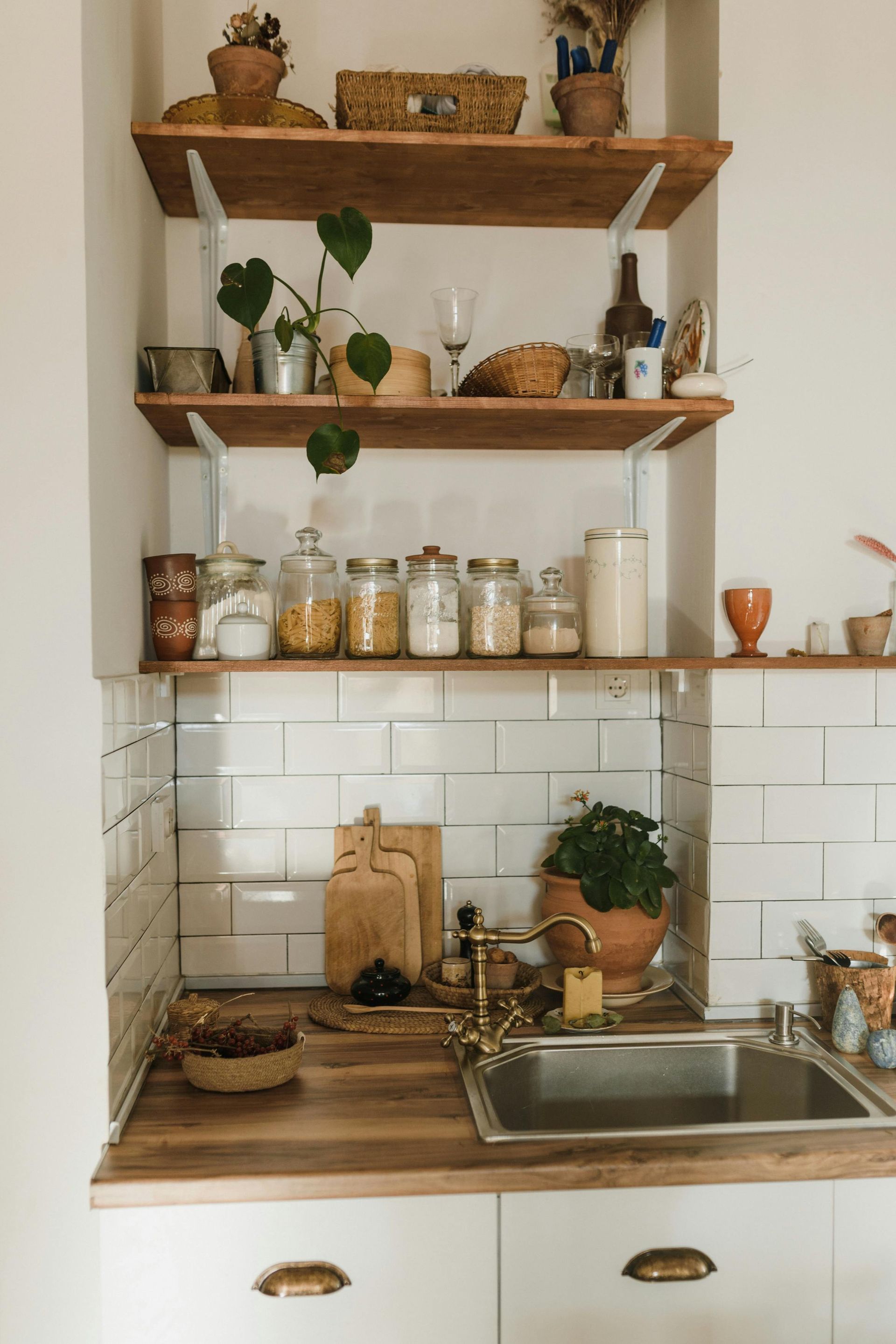 A cozy kitchen with wooden shelves and countertops, featuring jars, plants, and a stainless steel sink.