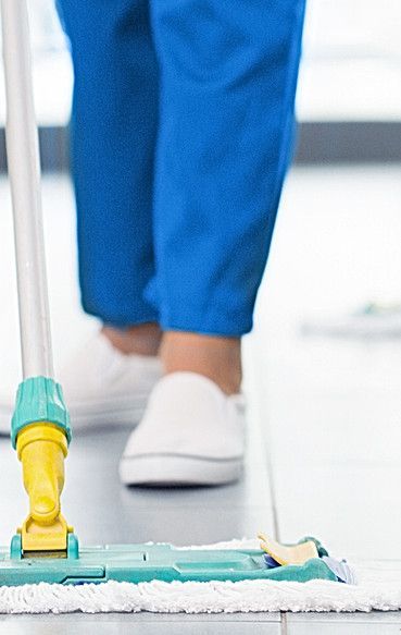 Person in blue pants and white shoes mopping a tile floor.