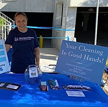 Woman at Horizon West Cleaning services booth, blue tablecloth, sign reads
