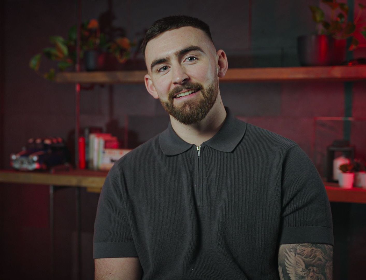 A man with a beard is sitting in front of a shelf and smiling.