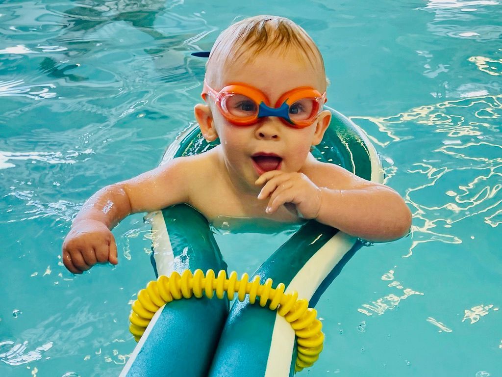 A baby wearing goggles is swimming in a pool.