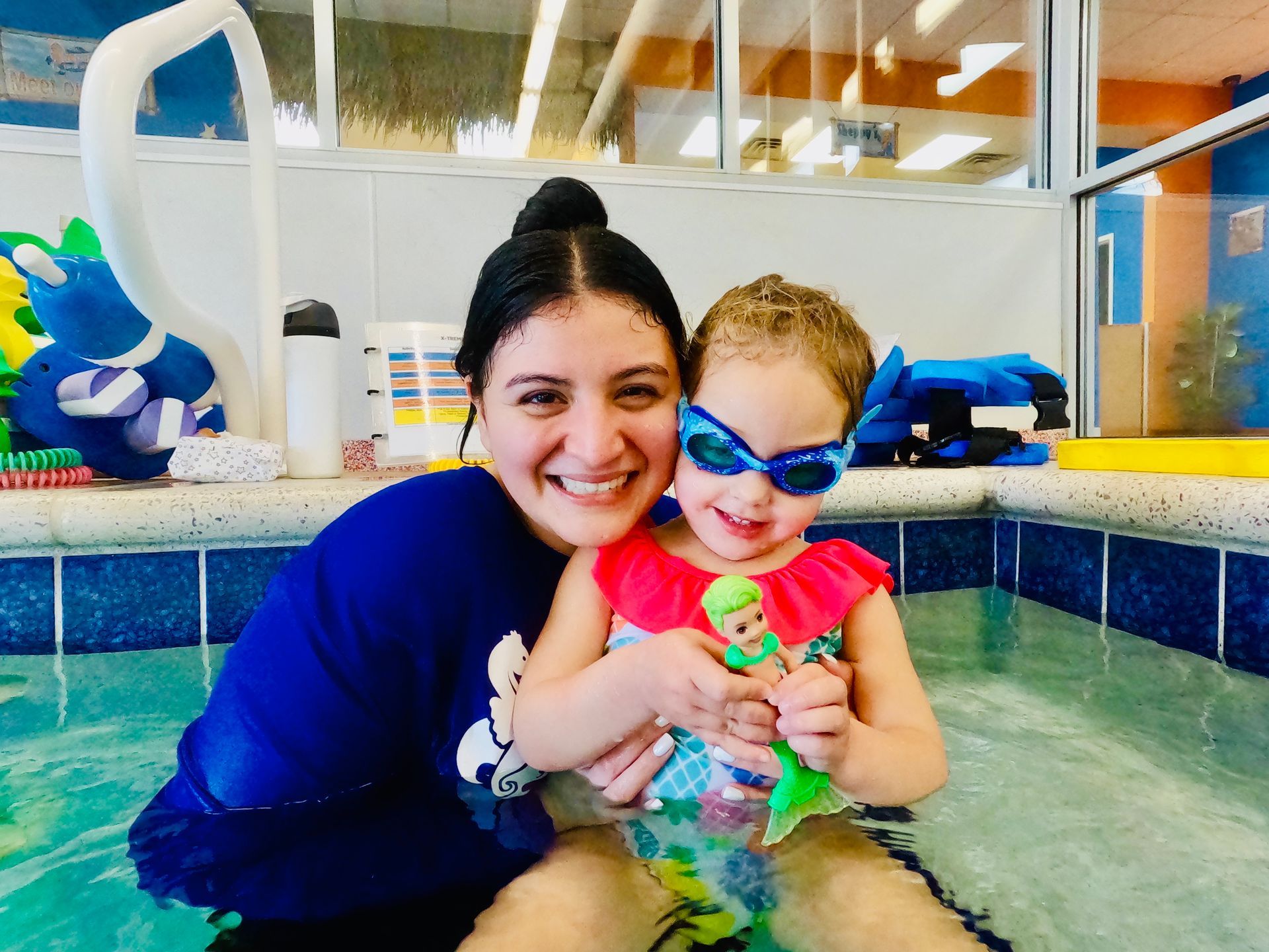 A woman is holding a little girl in a swimming pool.