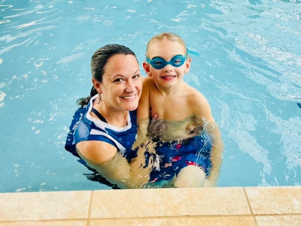A woman is holding a young boy in a swimming pool.
