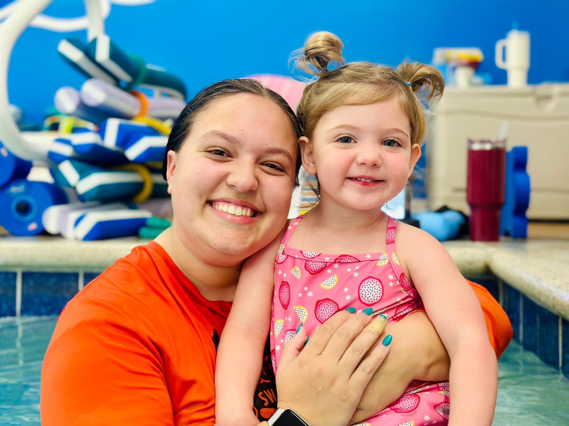 A woman is holding a little girl in her arms in a swimming pool.