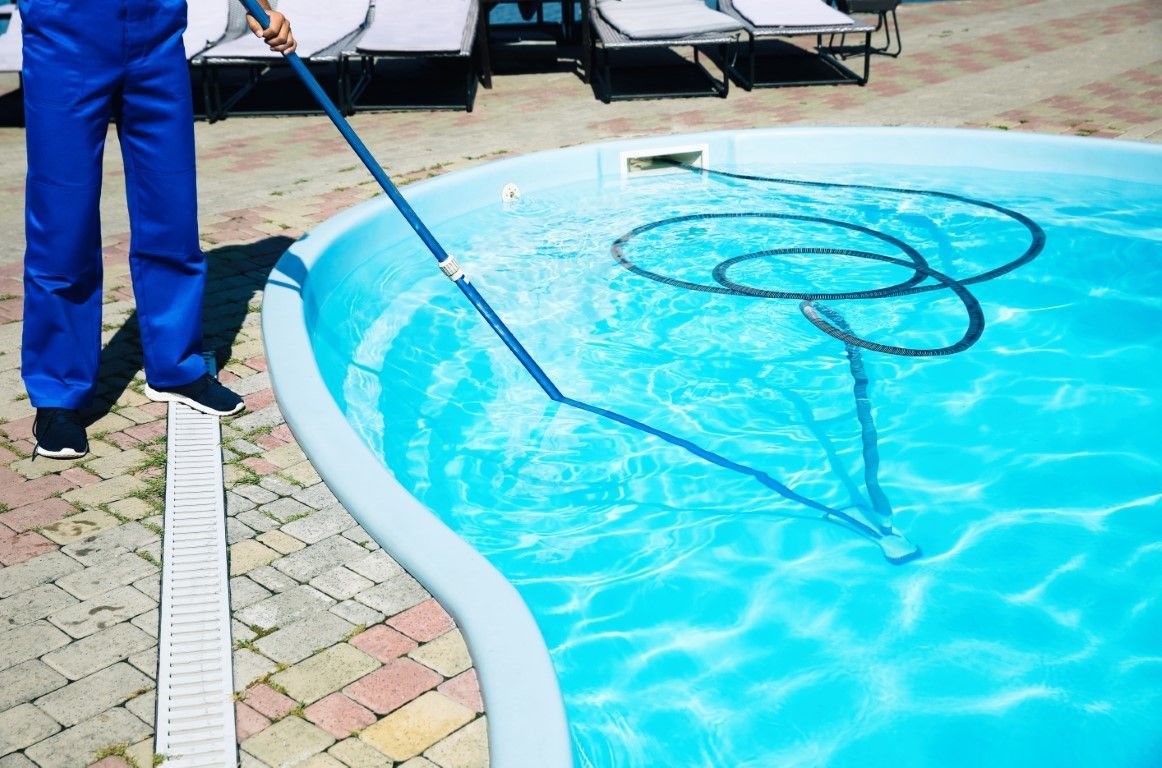 Person cleaning a small pool with a blue hose, creating dark debris loops in the water.