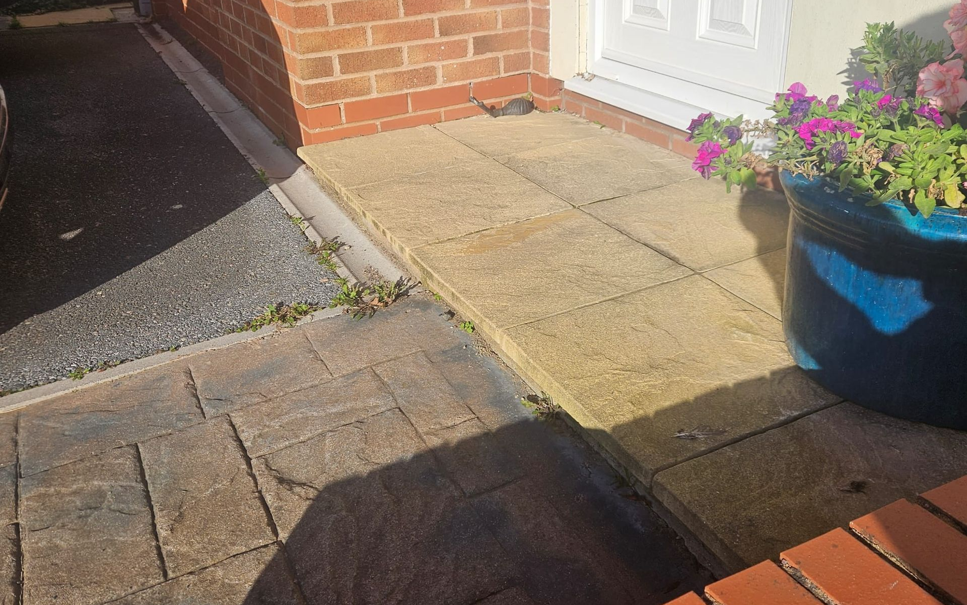 Beige paving slabs leading to a front door with a blue flower pot on the right. Brickwork surrounds.