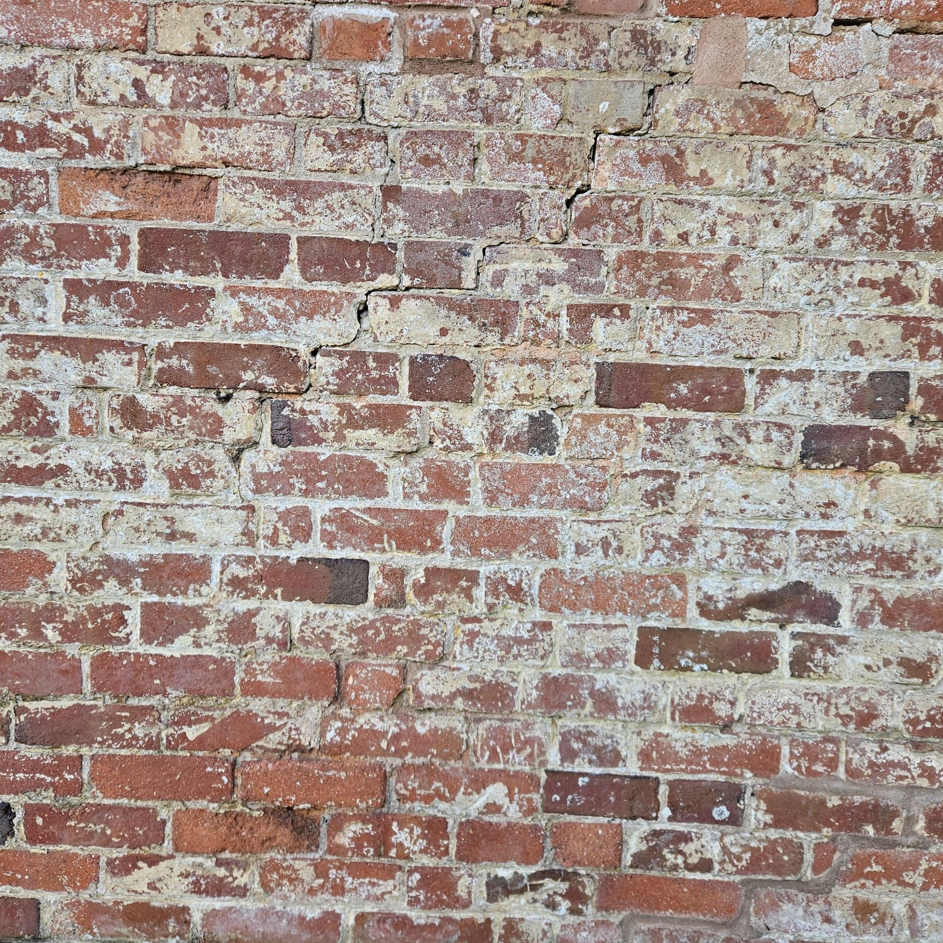 Weathered brick wall, red and brown bricks with white mortar, some cracks present.