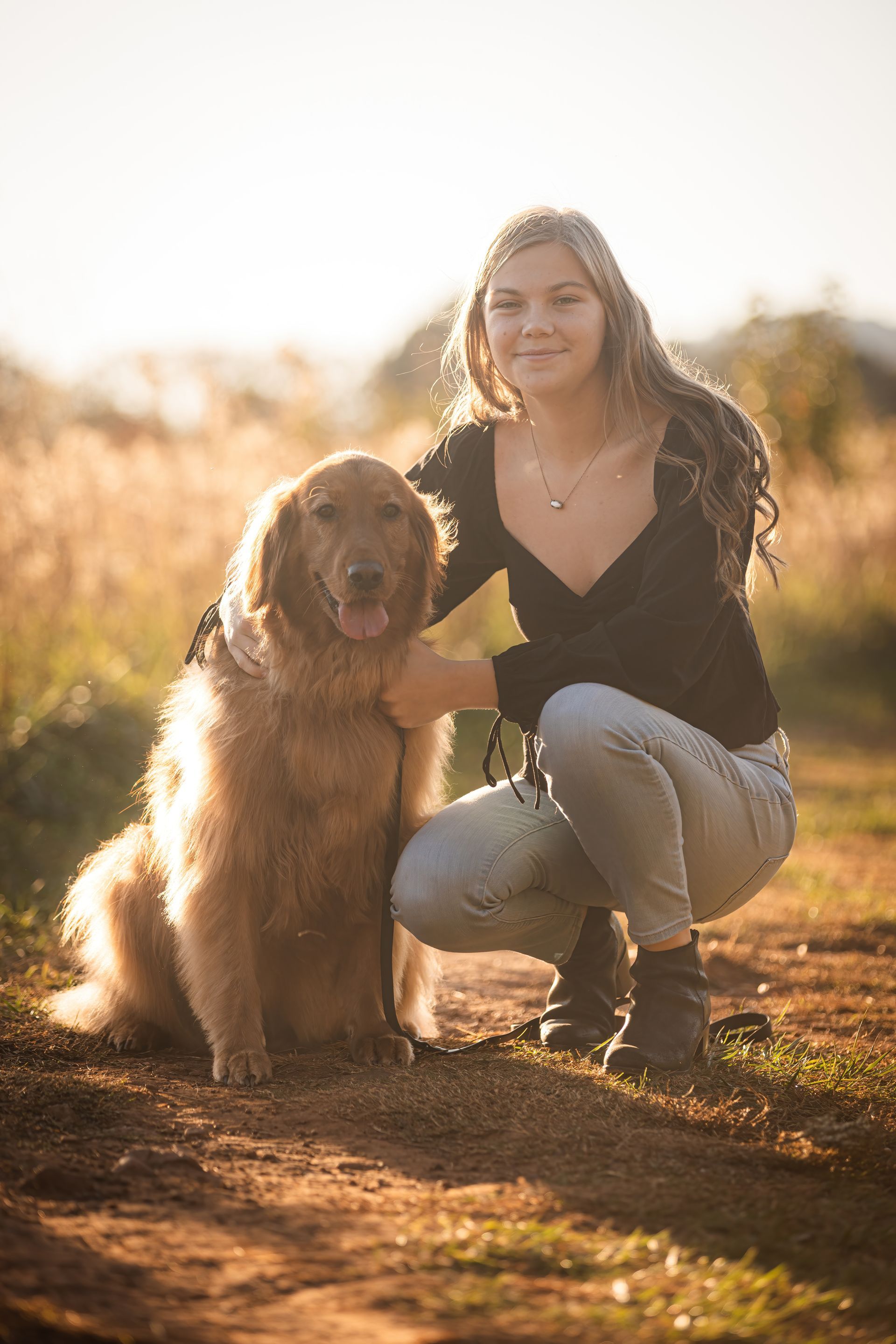A woman is kneeling down next to a dog in a field.