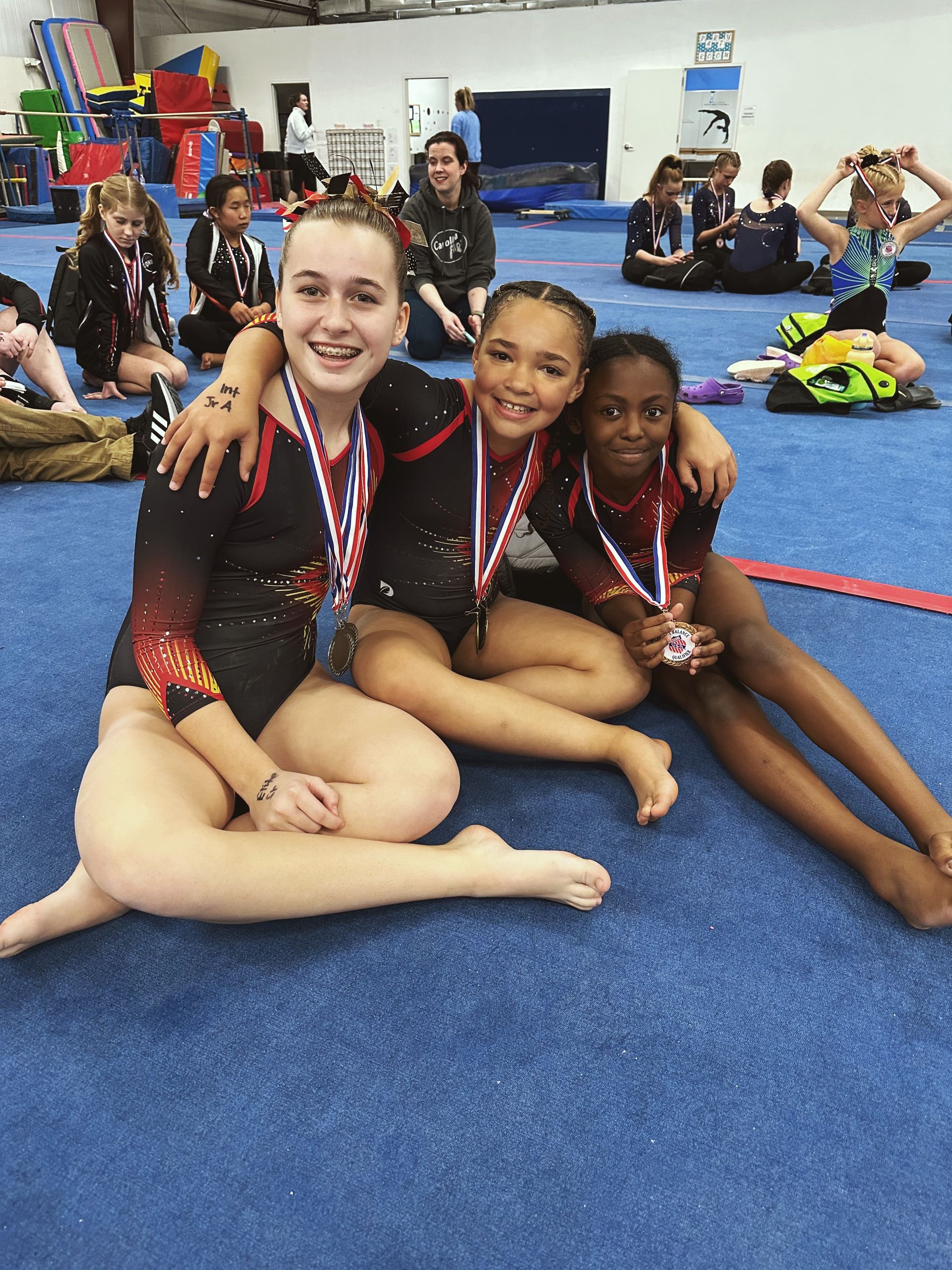 Three young girls are sitting on the floor with medals around their necks.