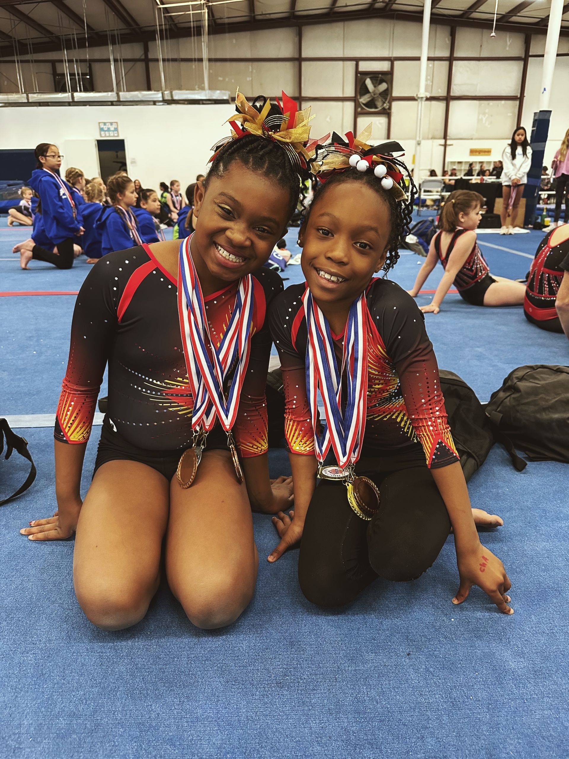 Two young girls are sitting on the floor with medals around their necks.