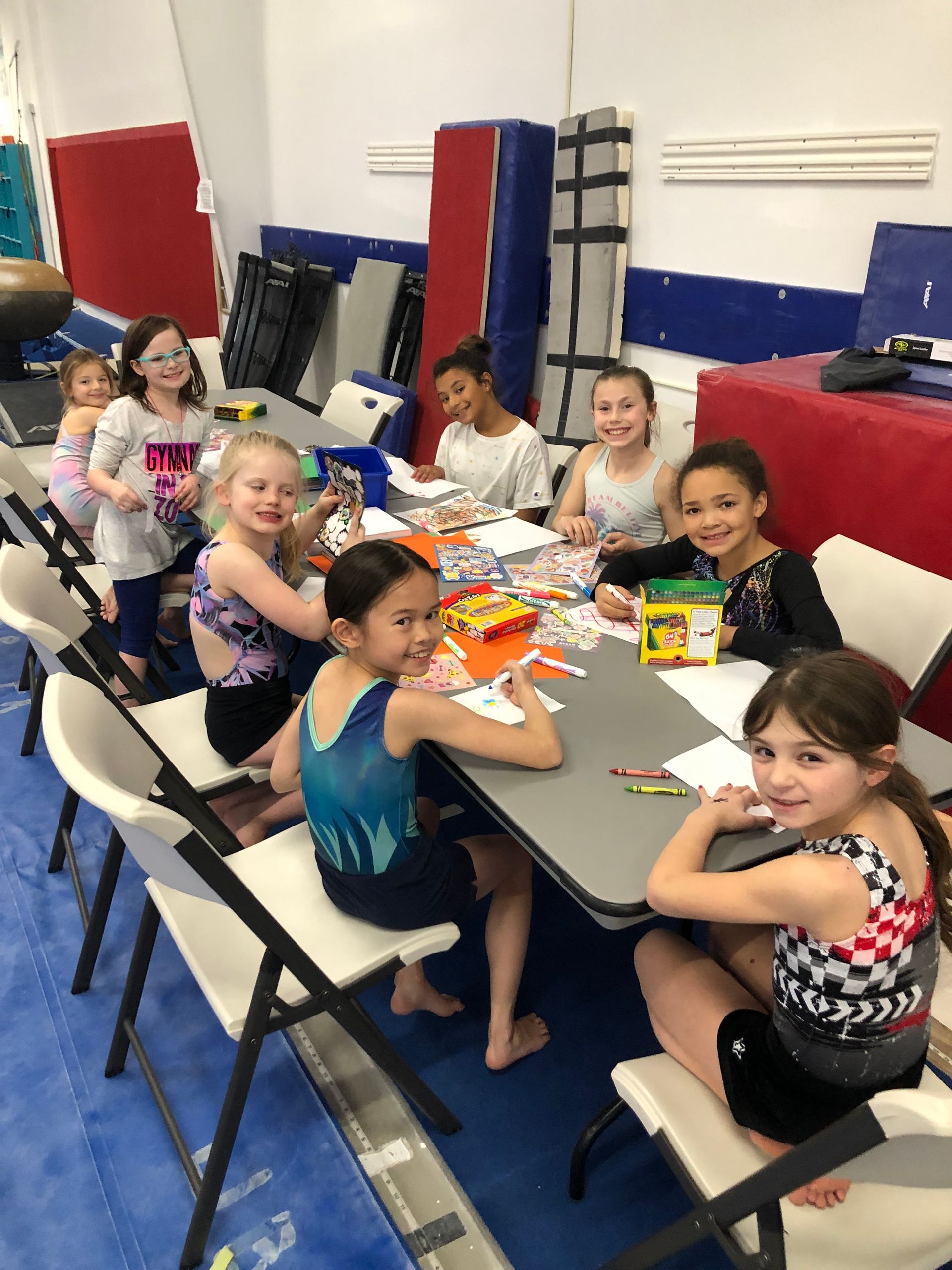 A group of young girls are sitting around a table in a gym.