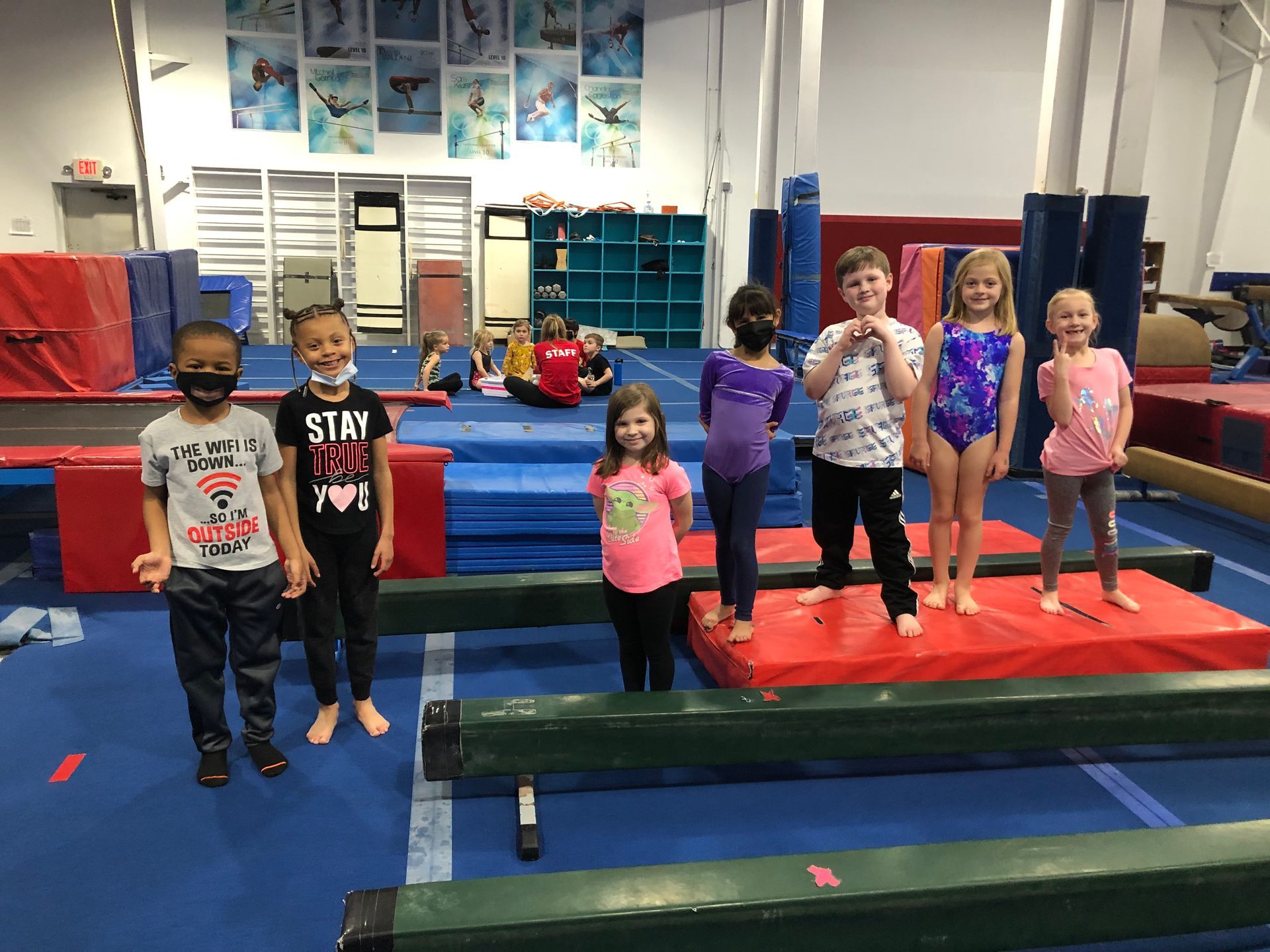 A group of children are standing on balance beam in a gym.