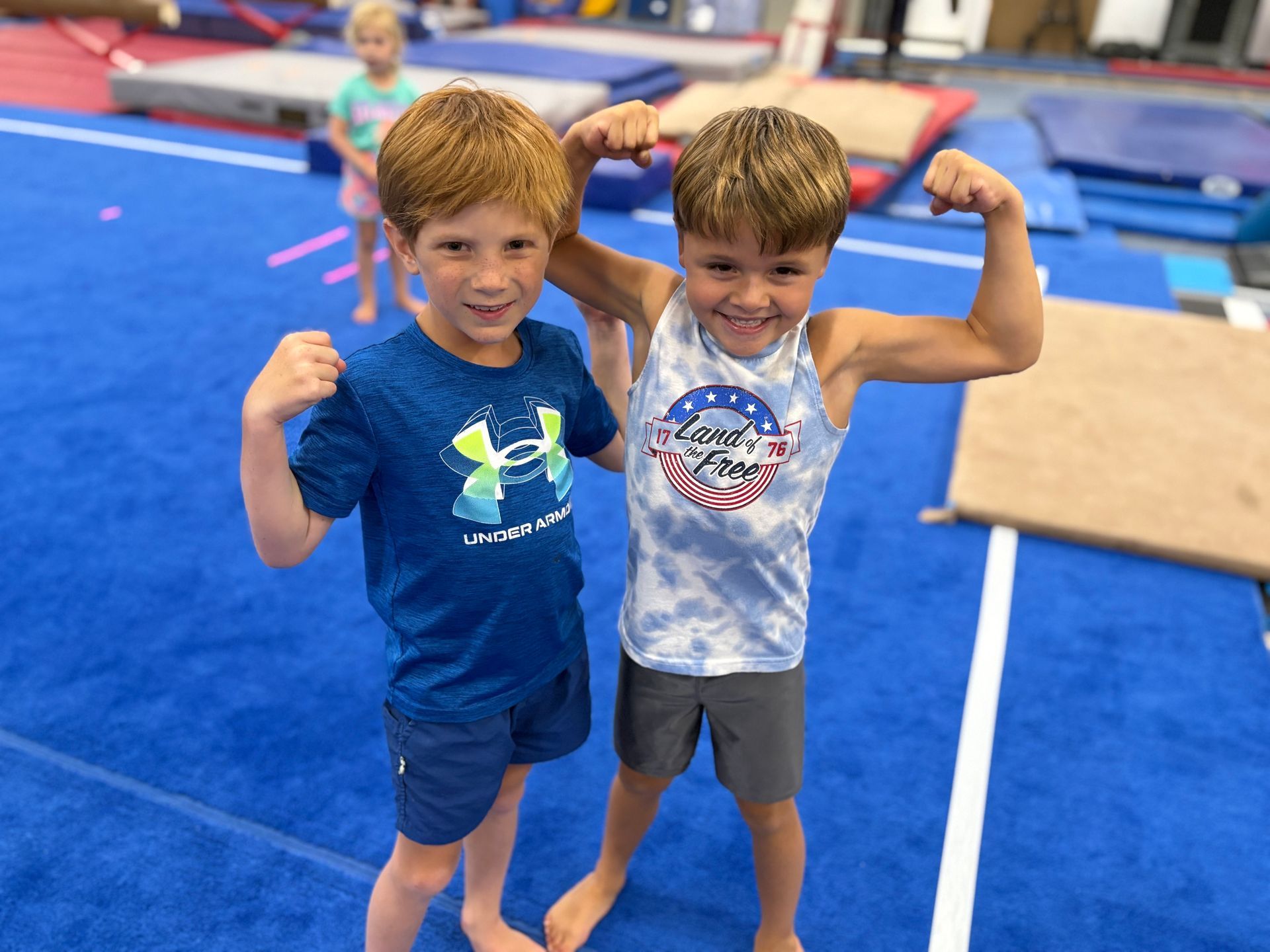 Two young boys are flexing their muscles in a gym.