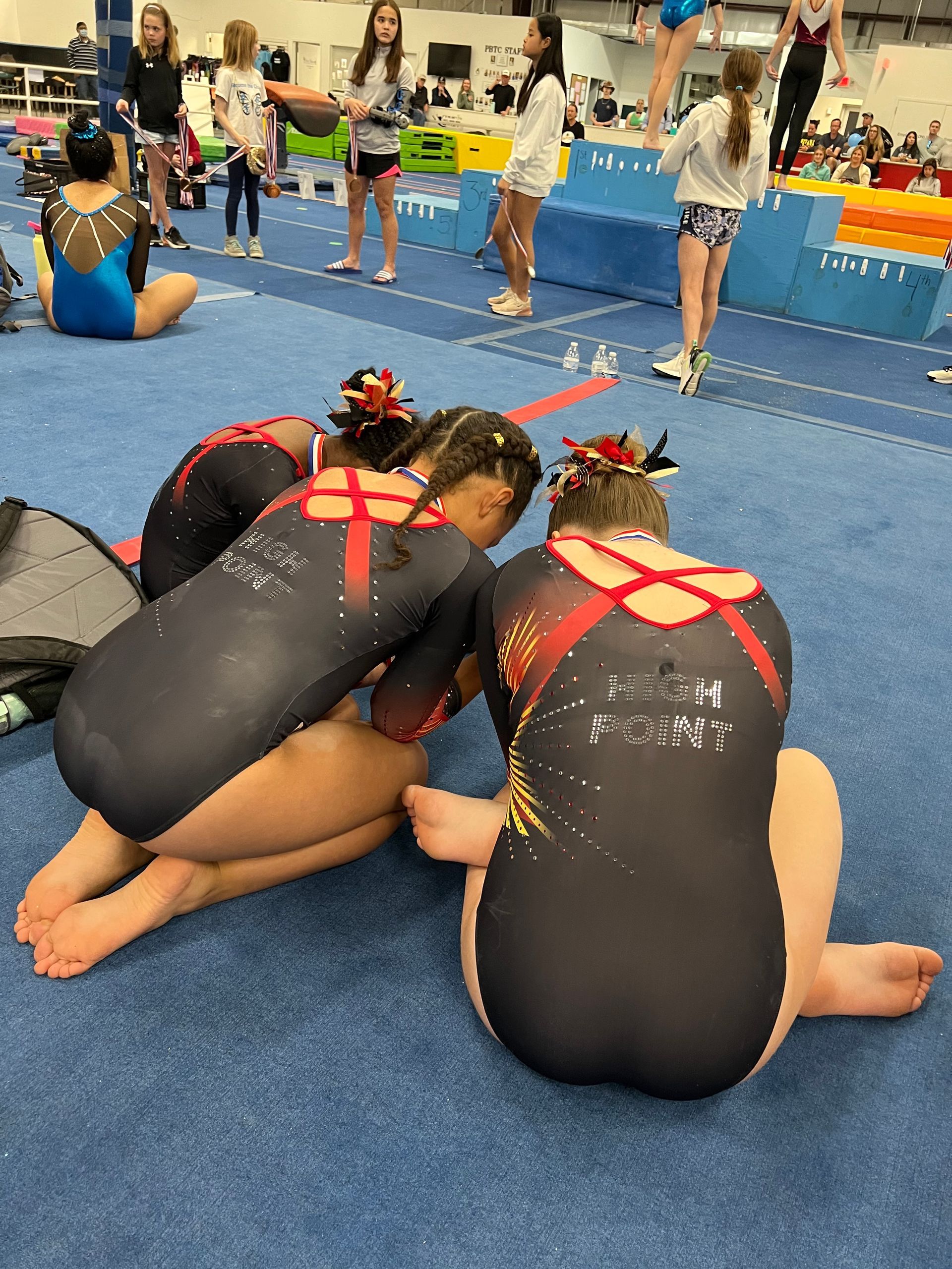 A group of female gymnasts are kneeling on the floor in a gym.