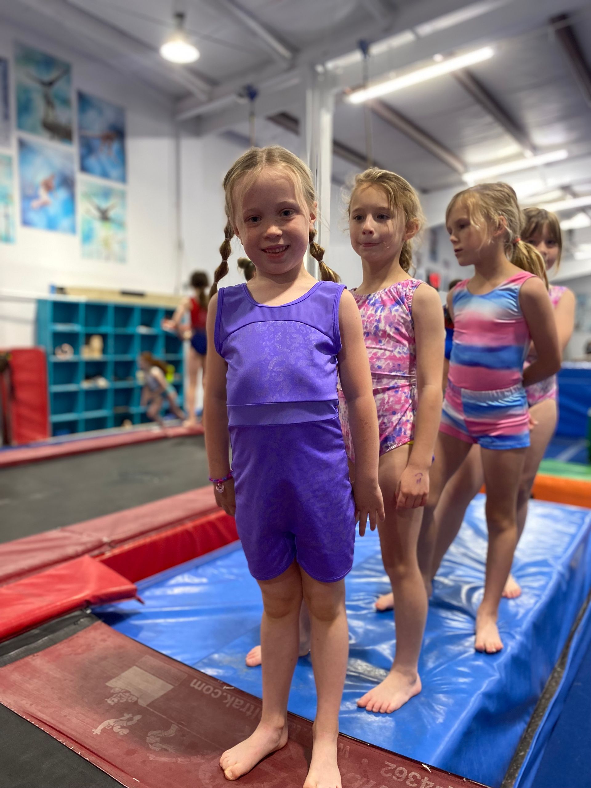 A group of young girls are standing on a trampoline in a gym.